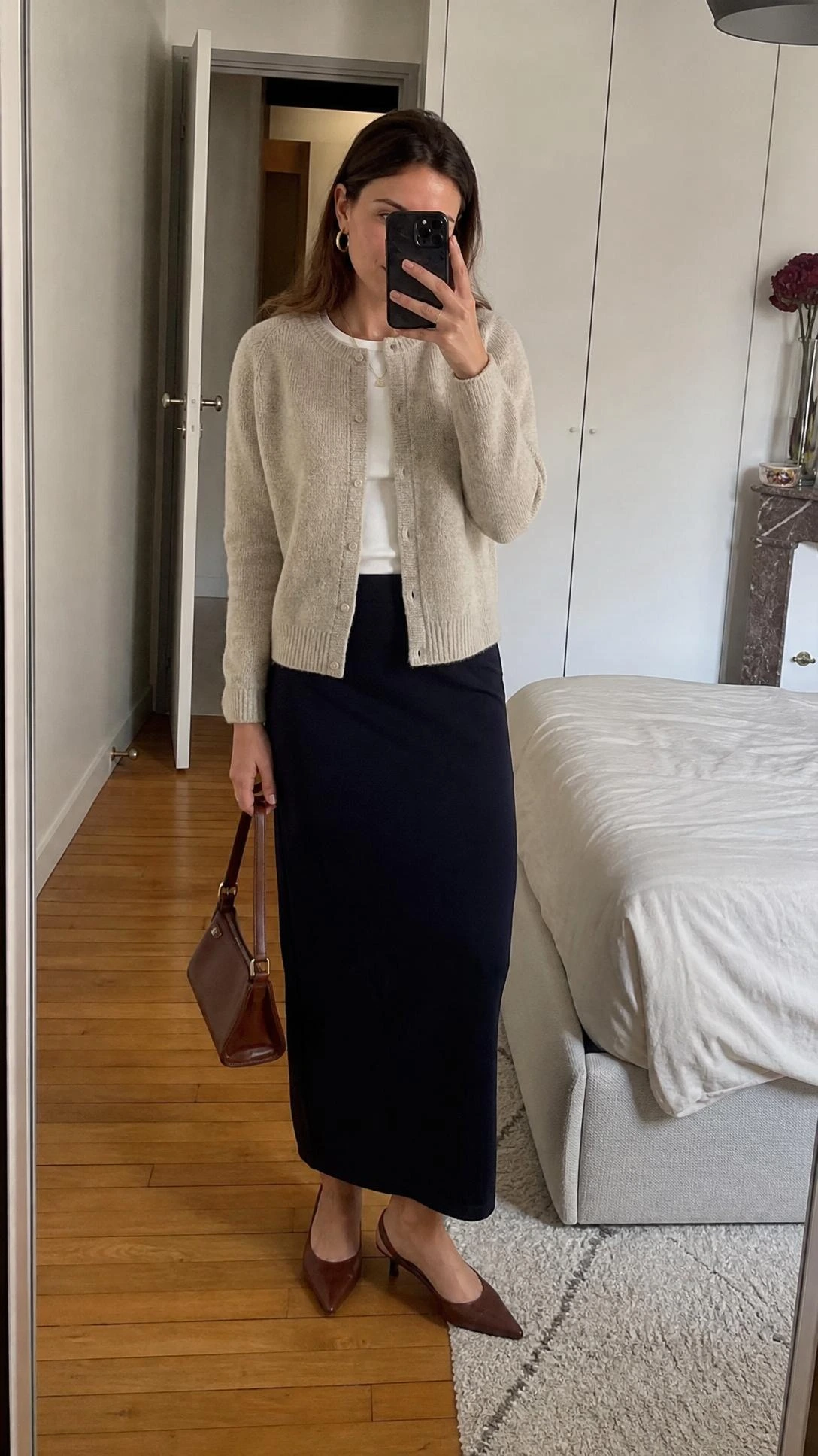 Mirror selfie of a woman in a fine knit cardigan and ankle-length column skirt, a chic parisian office outfit indoors.