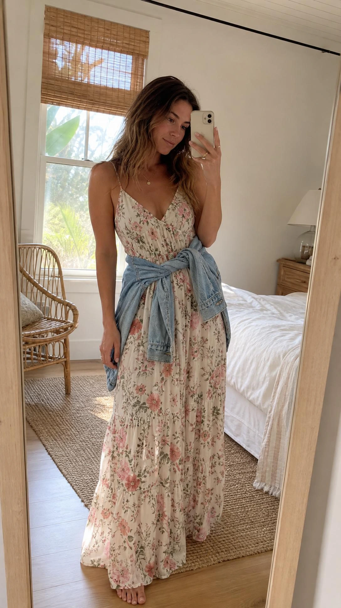 Woman in a pastel floral maxi dress with a light-wash denim jacket tied at the waist — a modest beach outfit that blends bohemian ease with coverage