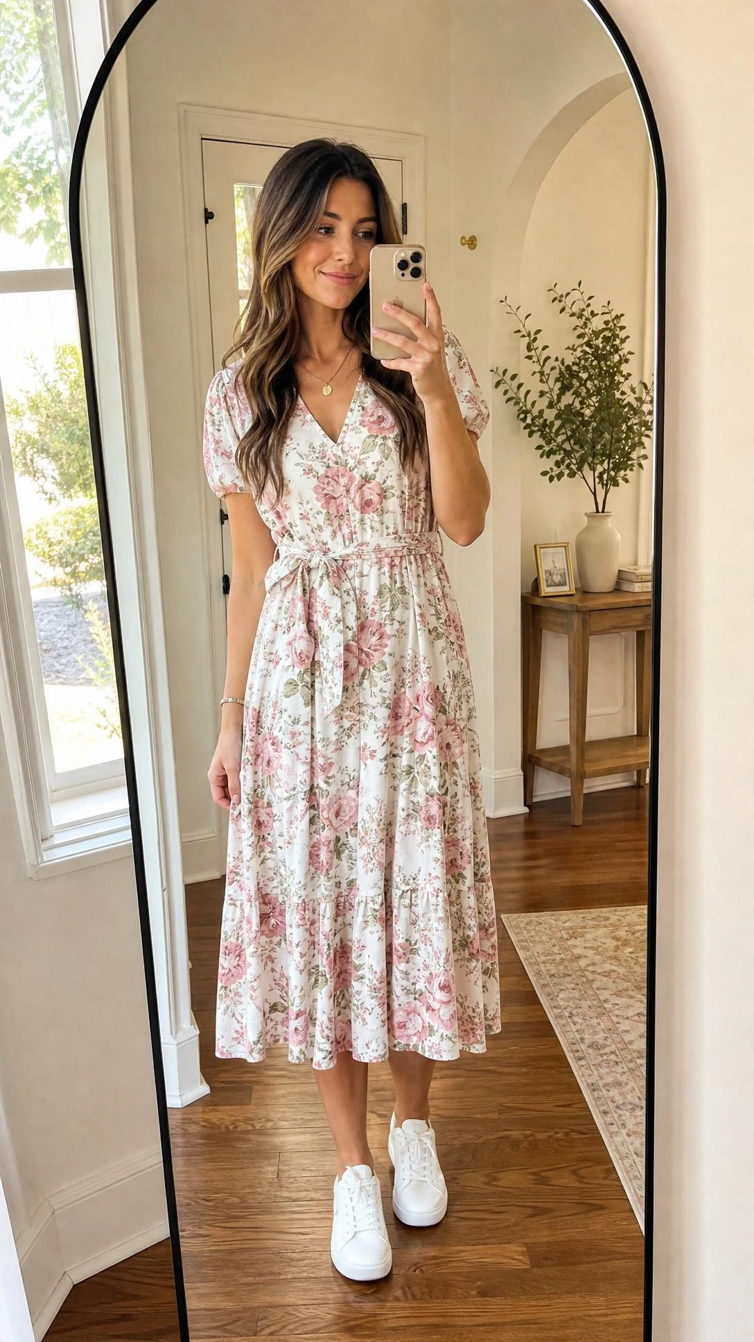 Young woman in a floral midi dress paired with crisp white sneakers takes a mirror selfie in a sunlit entryway, showing a casual yet polished brunch outfit