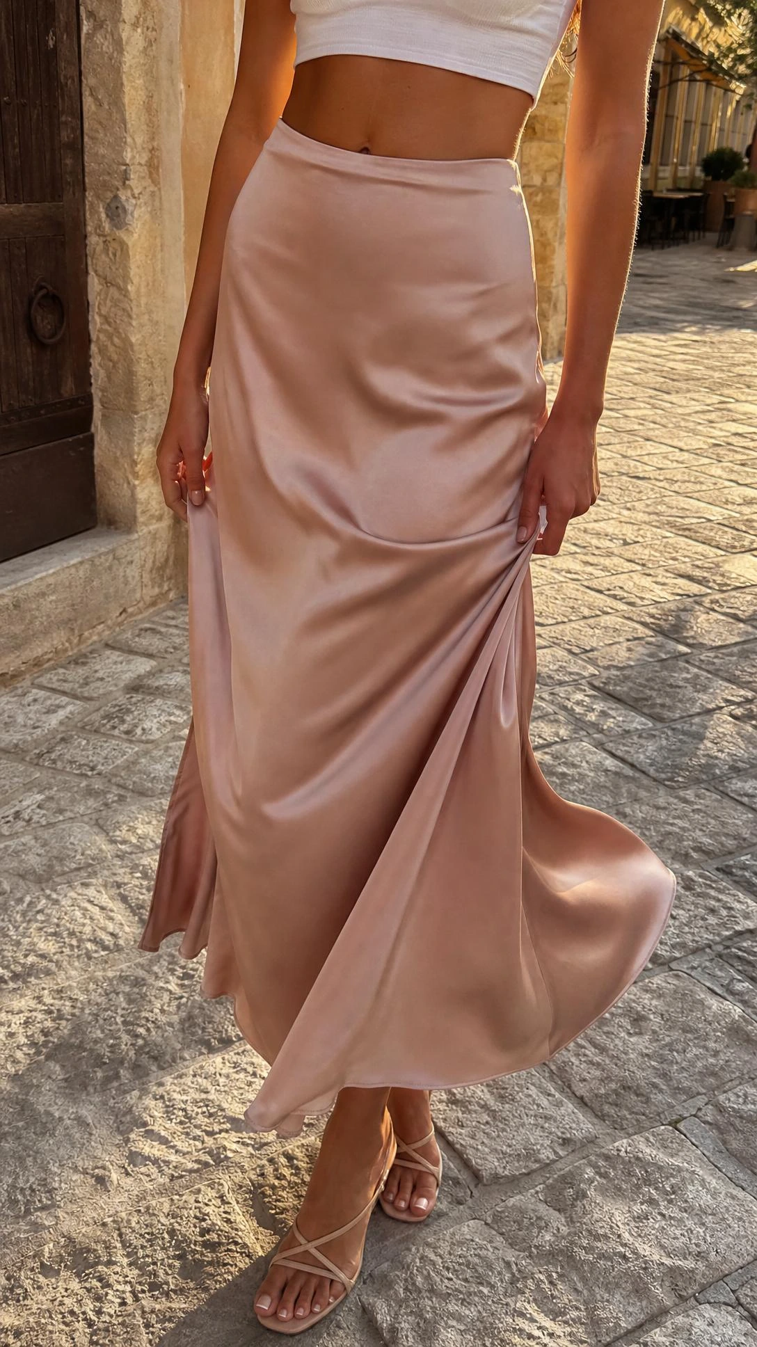 Satin maxi skirt in champagne paired with a white cropped tee, waist-down shot showing the luxurious fabric drape in warm afternoon light