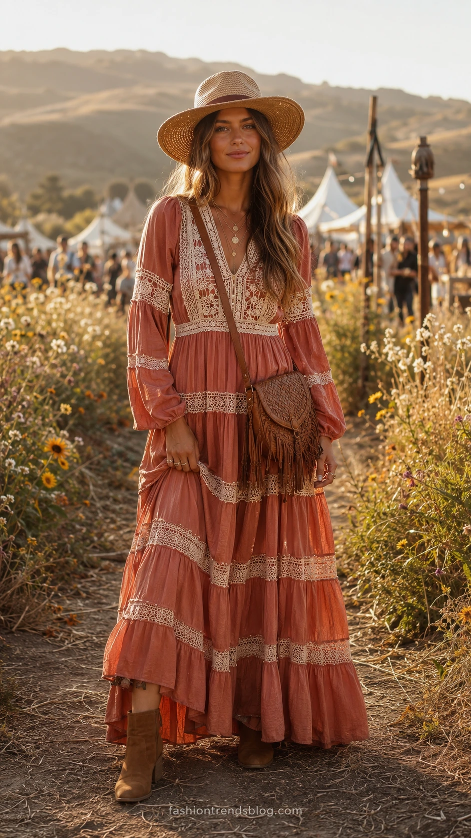 Woman wearing a flowing tiered maxi dress with ivory crochet inserts in terracotta and dusty rose, standing on a sunlit festival pathway surrounded by wildflowers