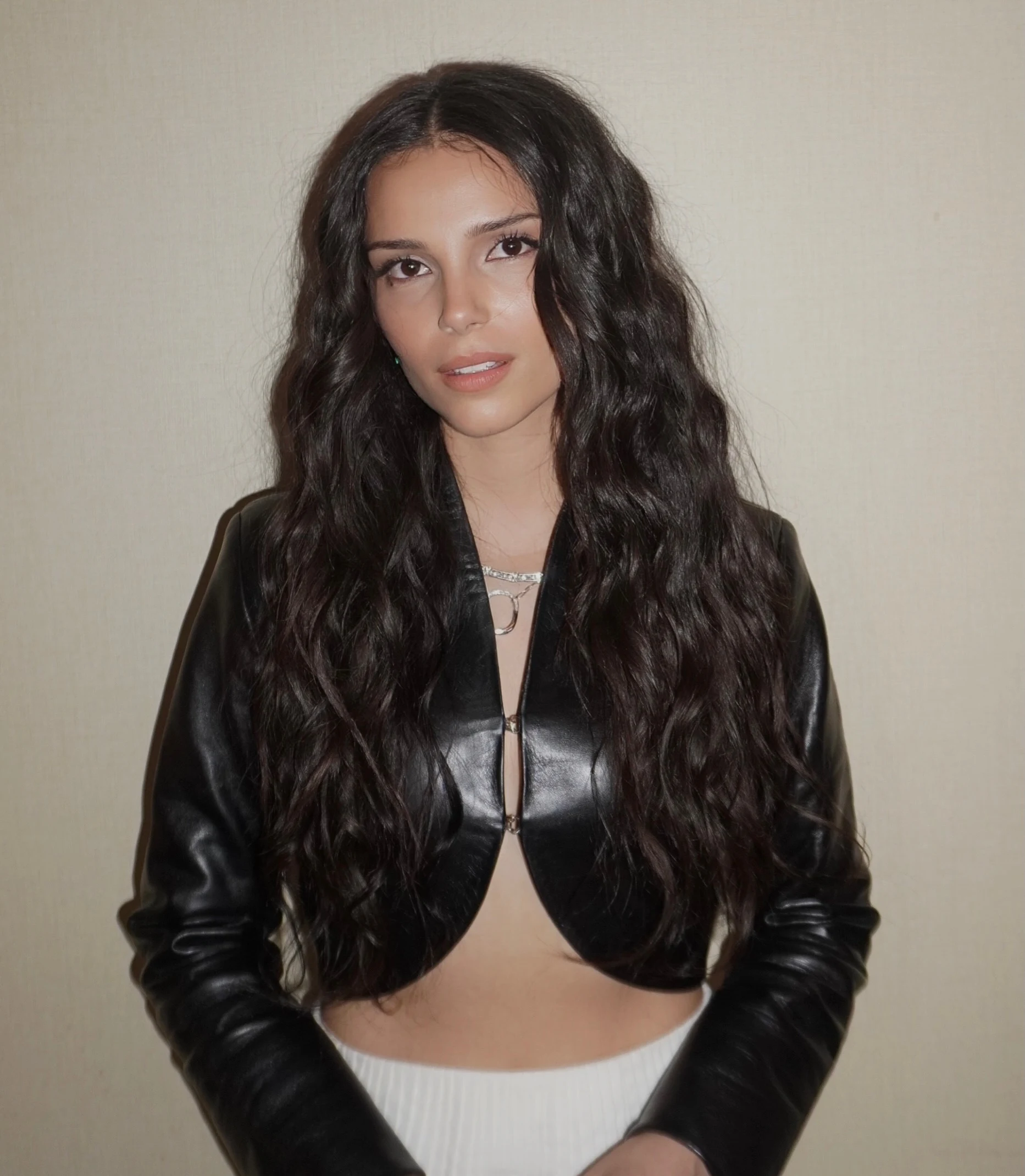 Glossy black cropped jacket worn open over a bare midriff with a high-waisted white skirt.