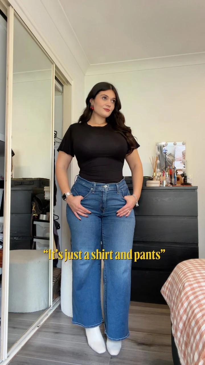 Person wearing a black short-sleeve top, medium-blue straight-leg jeans, and white pointed-toe shoes.