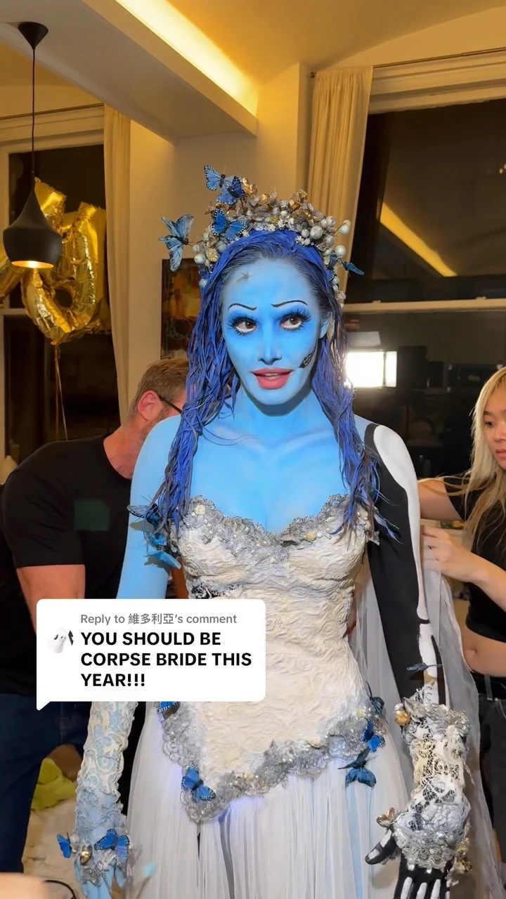 Person in full blue body paint wearing a blue dress with a pearl and butterfly crown.