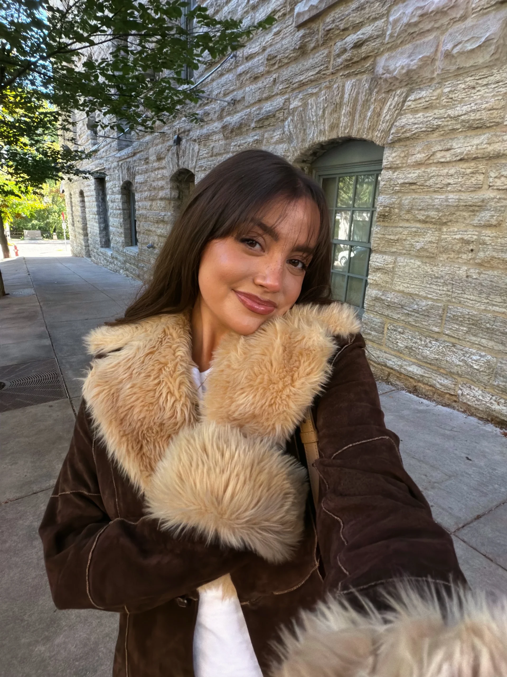 Dark brown jacket with oversized cream fluffy trim at collar and cuffs over a white top.