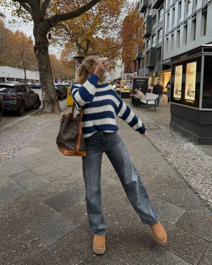 This outfit features a chunky striped knit sweater paired with relaxed wide-leg jeans for a comfy yet stylish vibe. The look is completed with tan platform UGG boots and a brown leather tote, making it perfect for a casual stroll or coffee run.