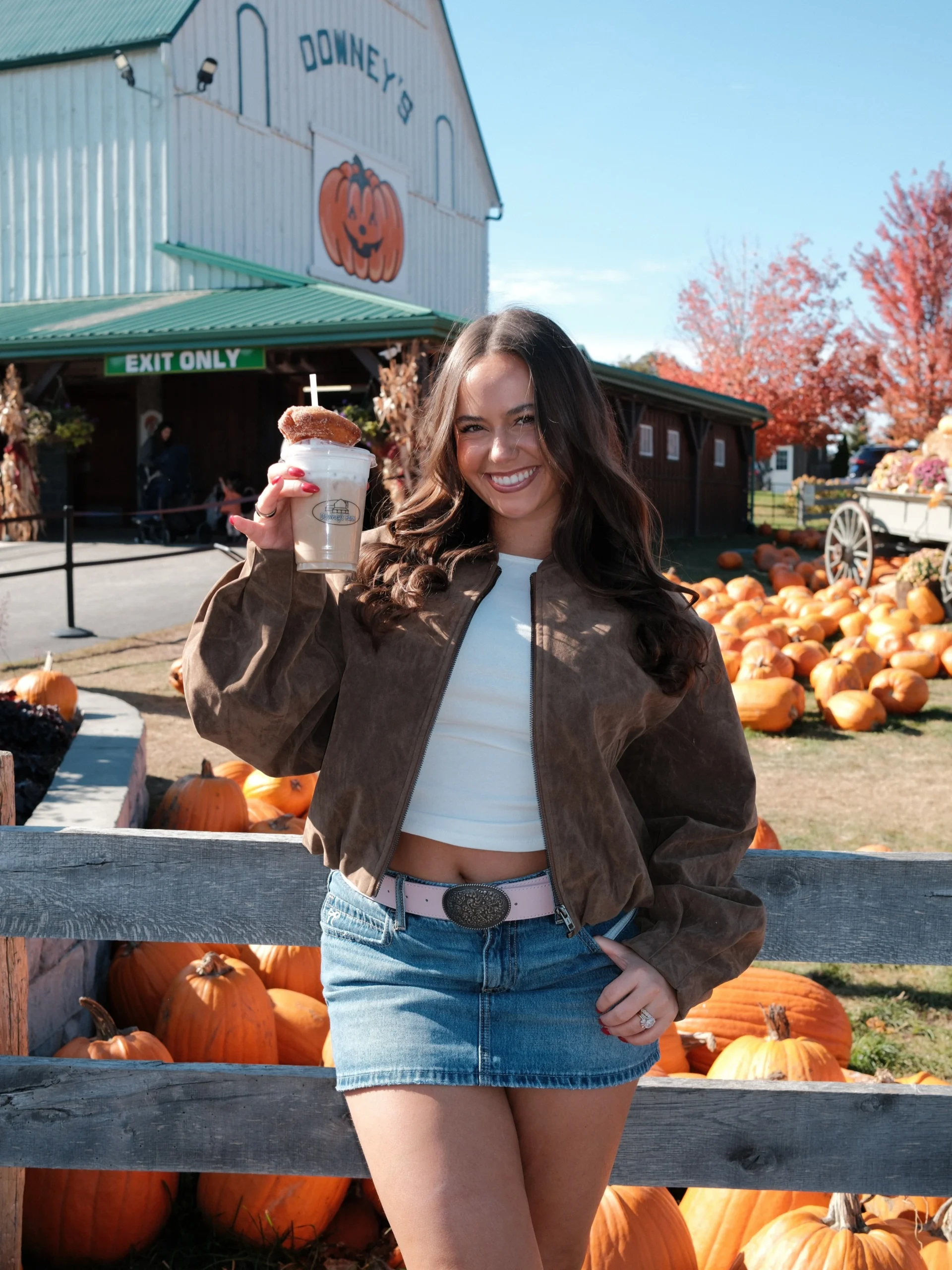 Brown cropped suede jacket, white top, denim mini skirt, and brown knee-high boots fall fair outfit.