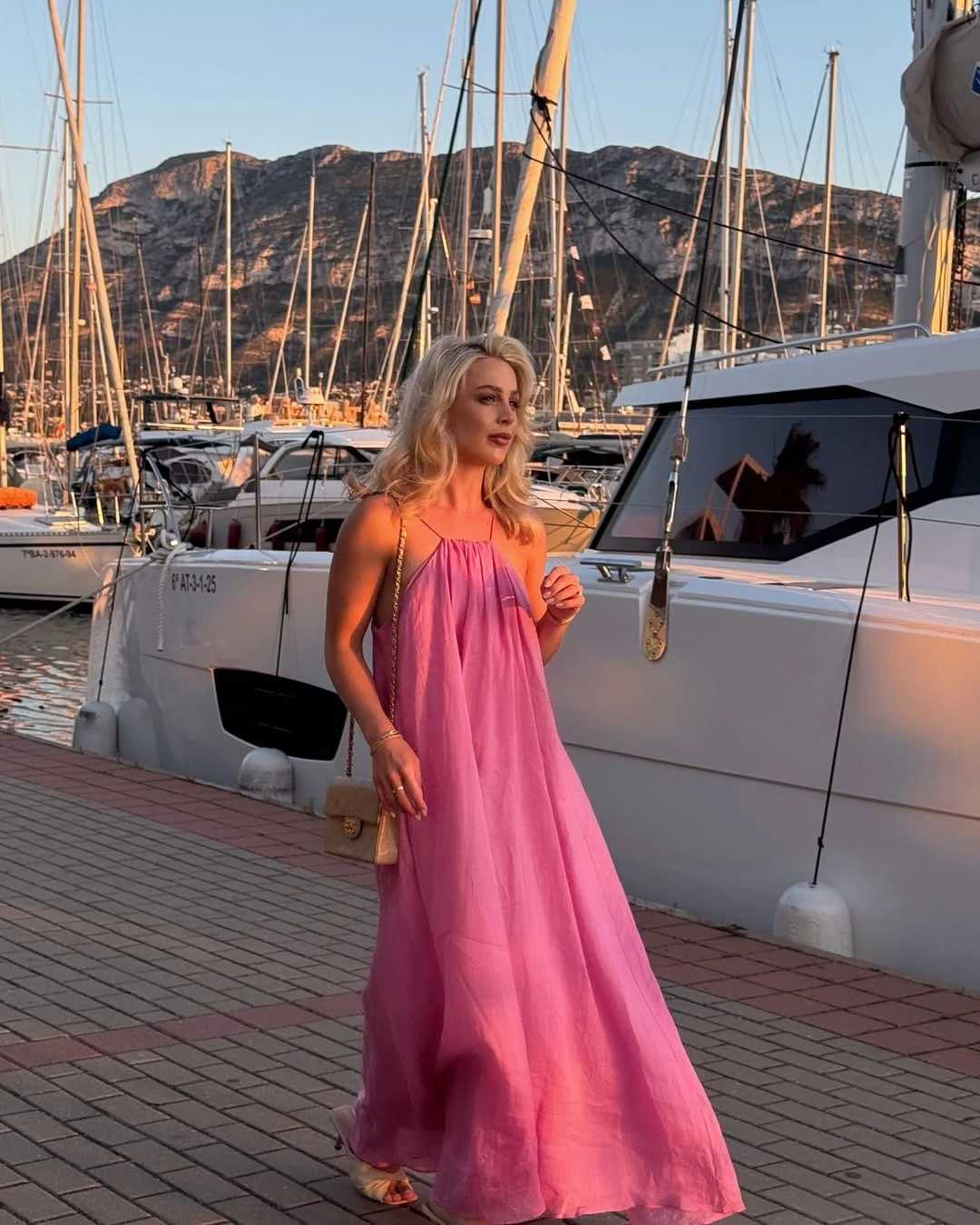via @allchloerose A flowing hot pink chiffon maxi dress with thin spaghetti straps and a voluminous A-line silhouette is finished with nude strappy sandals and a small gold quilted Chanel chain bag. The sheer, airy quality of the chiffon is what makes this dress so right for a cruise setting it catches the evening light and moves with the sea breeze in a way that no heavier fabric could replicate. I find this completely beautiful for a sunset harbour dinner when you want to look like the most memorable person on the dock. Recreate This Look
