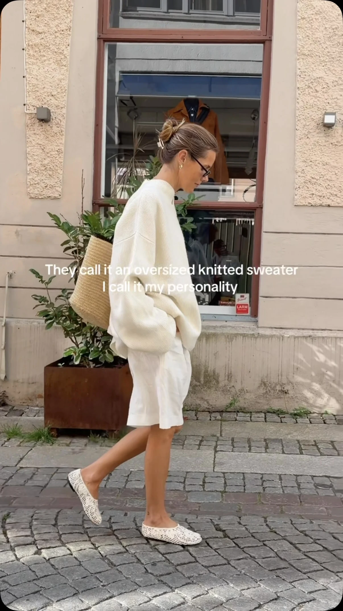 Oversized cream sweater with dropped shoulders paired with white pleated knee-length shorts.
