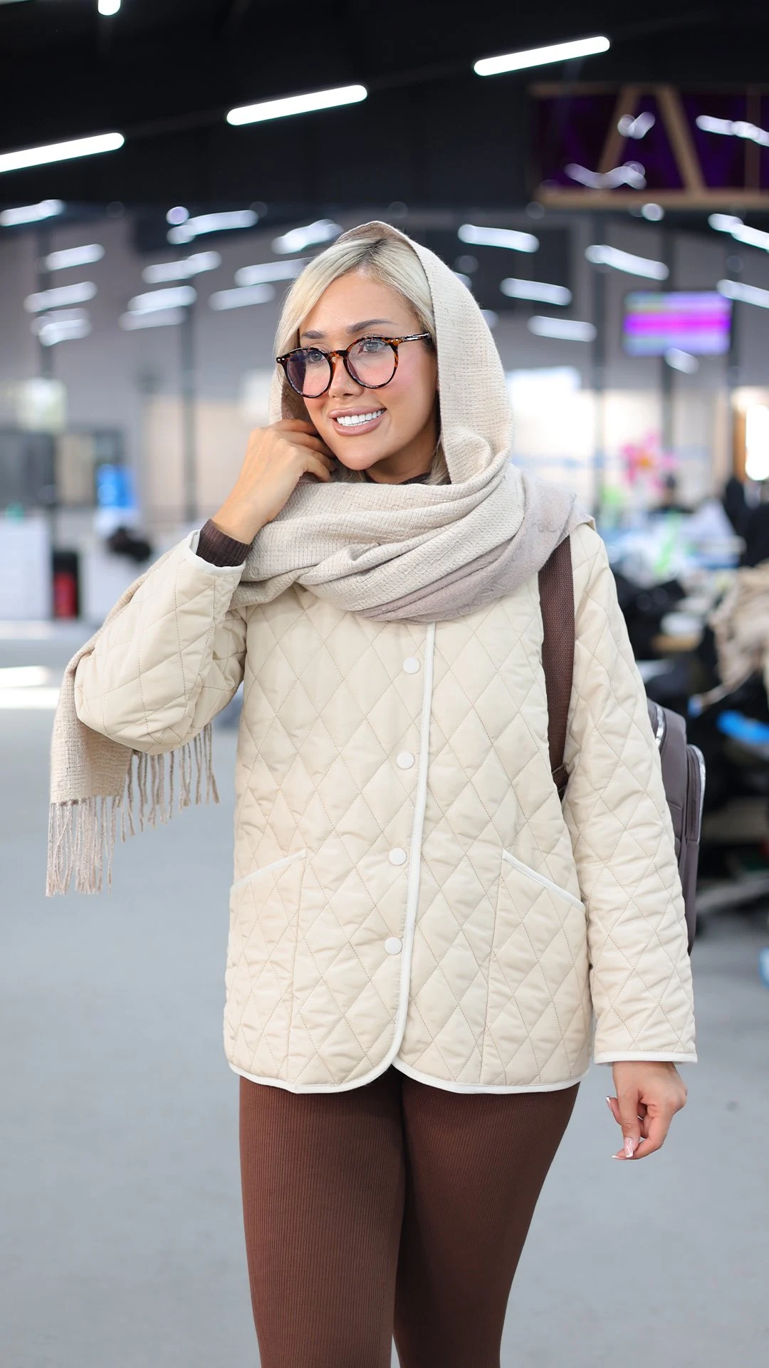 Person in cream quilted jacket, beige-gray fringed scarf, and dark brown fitted trousers.