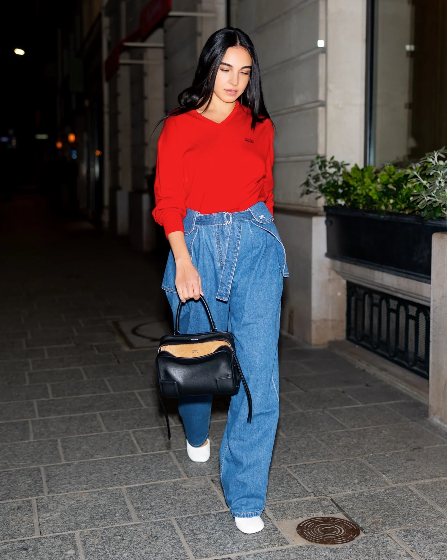 Red V-neck top tucked into wide-leg blue jeans with a denim belt, white shoes, and black handbag.