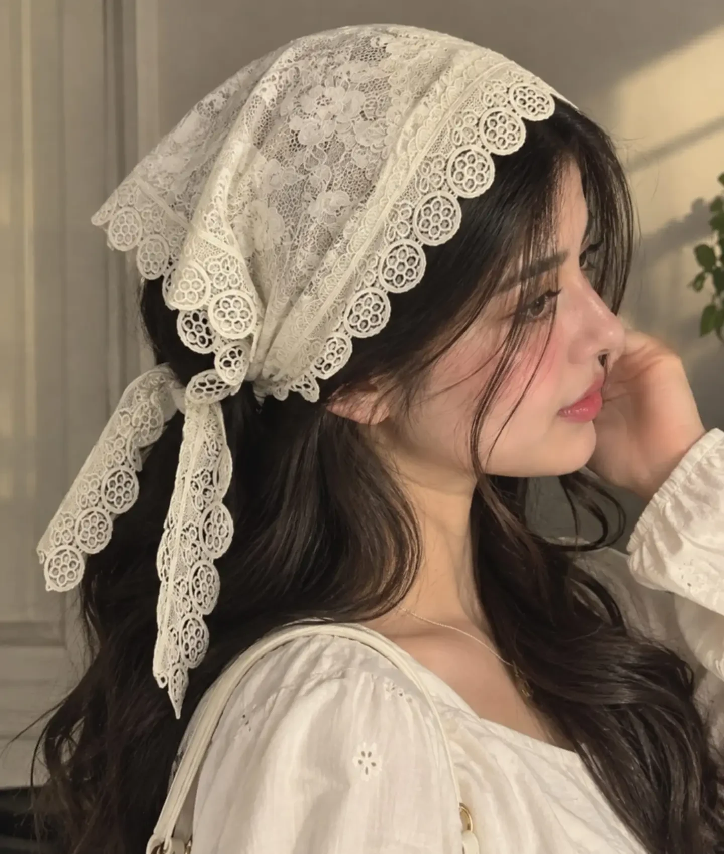 Woman wearing a cream lace headscarf tied at the back with a white puff sleeve embroidered blouse.