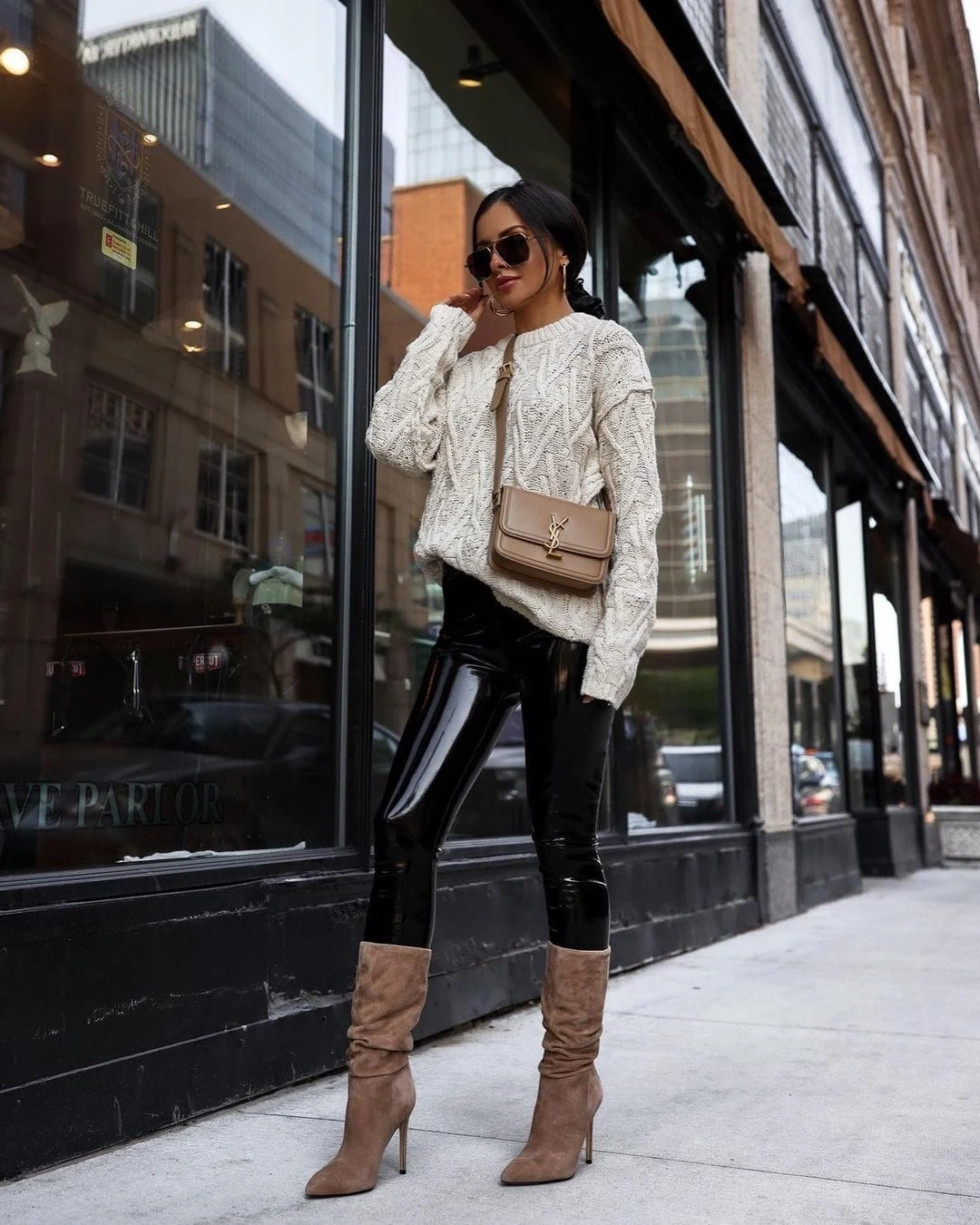 Woman wearing a white sweater, black leather pants, and boots in a casual chic outfit.