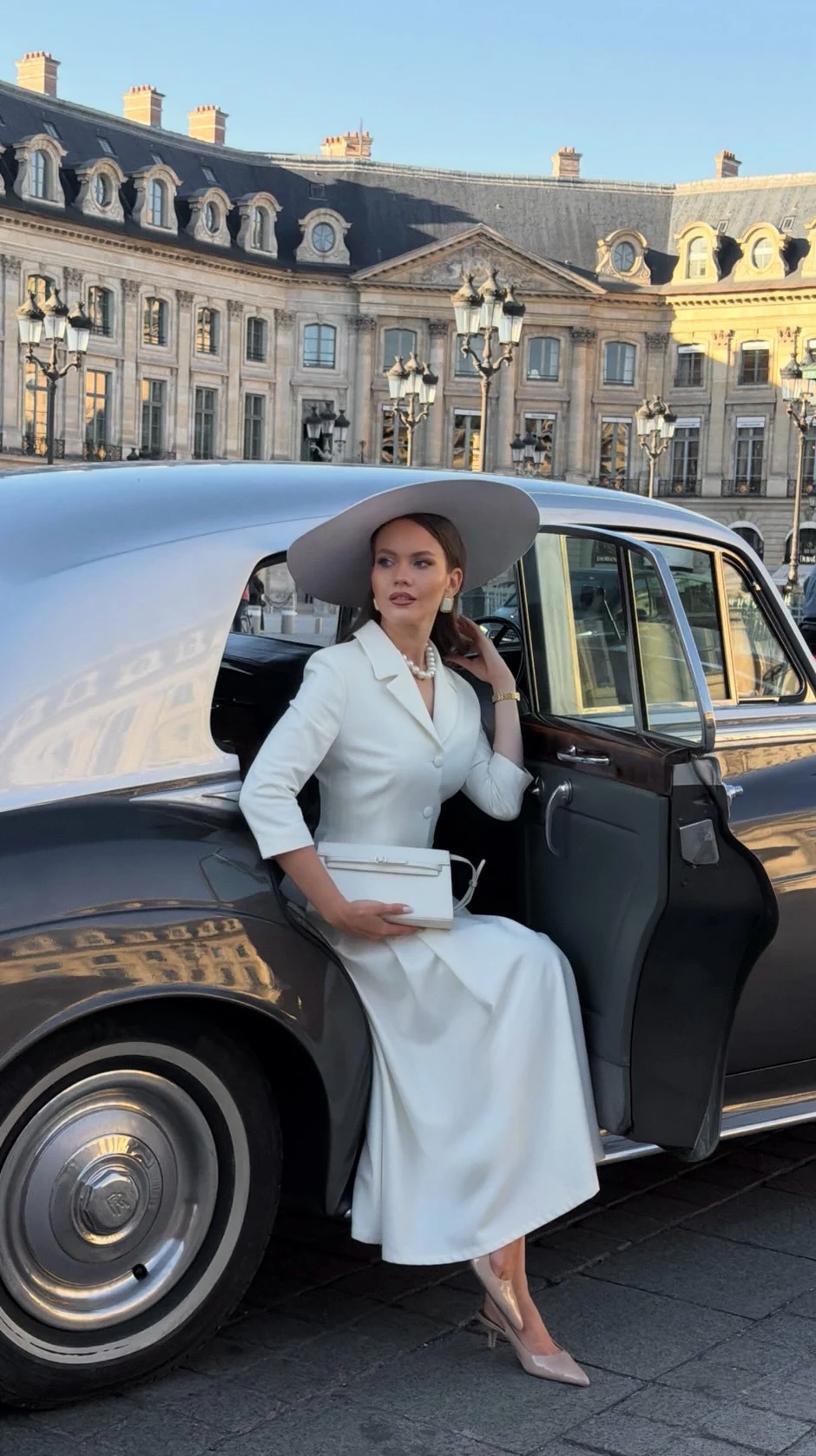 Woman in a white fitted jacket and long skirt wearing a gray hat and pale heels.