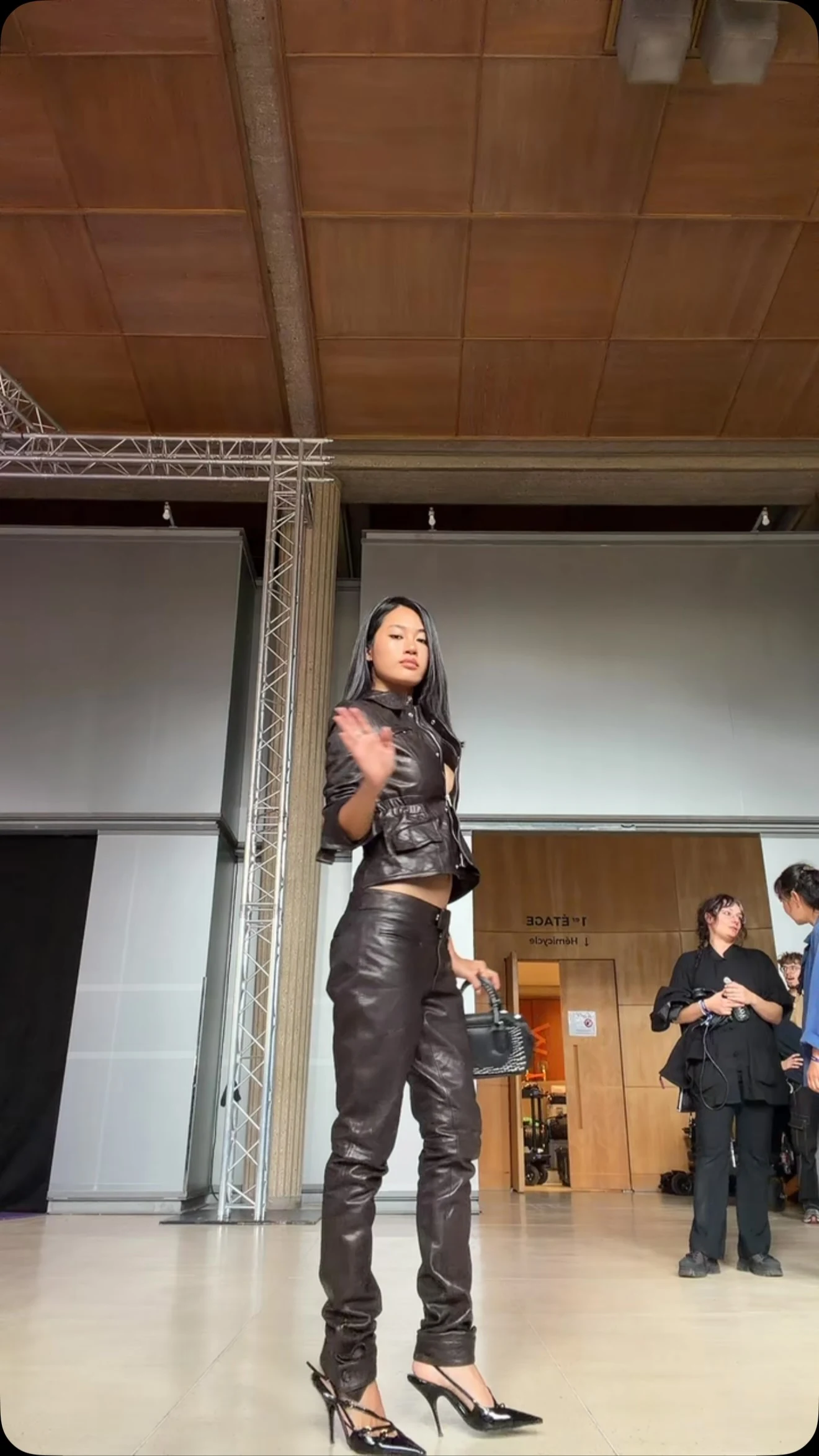 Fitted glossy black cropped jacket and matching high-waisted trousers with black pointed-toe heels.