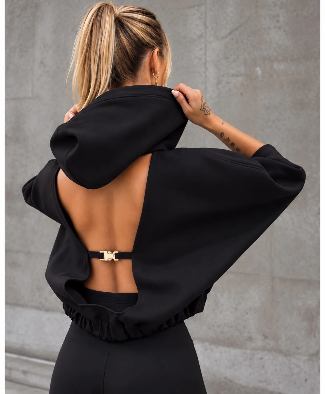Back view of a black open-back hooded top with wide sleeves paired with fitted black leggings.