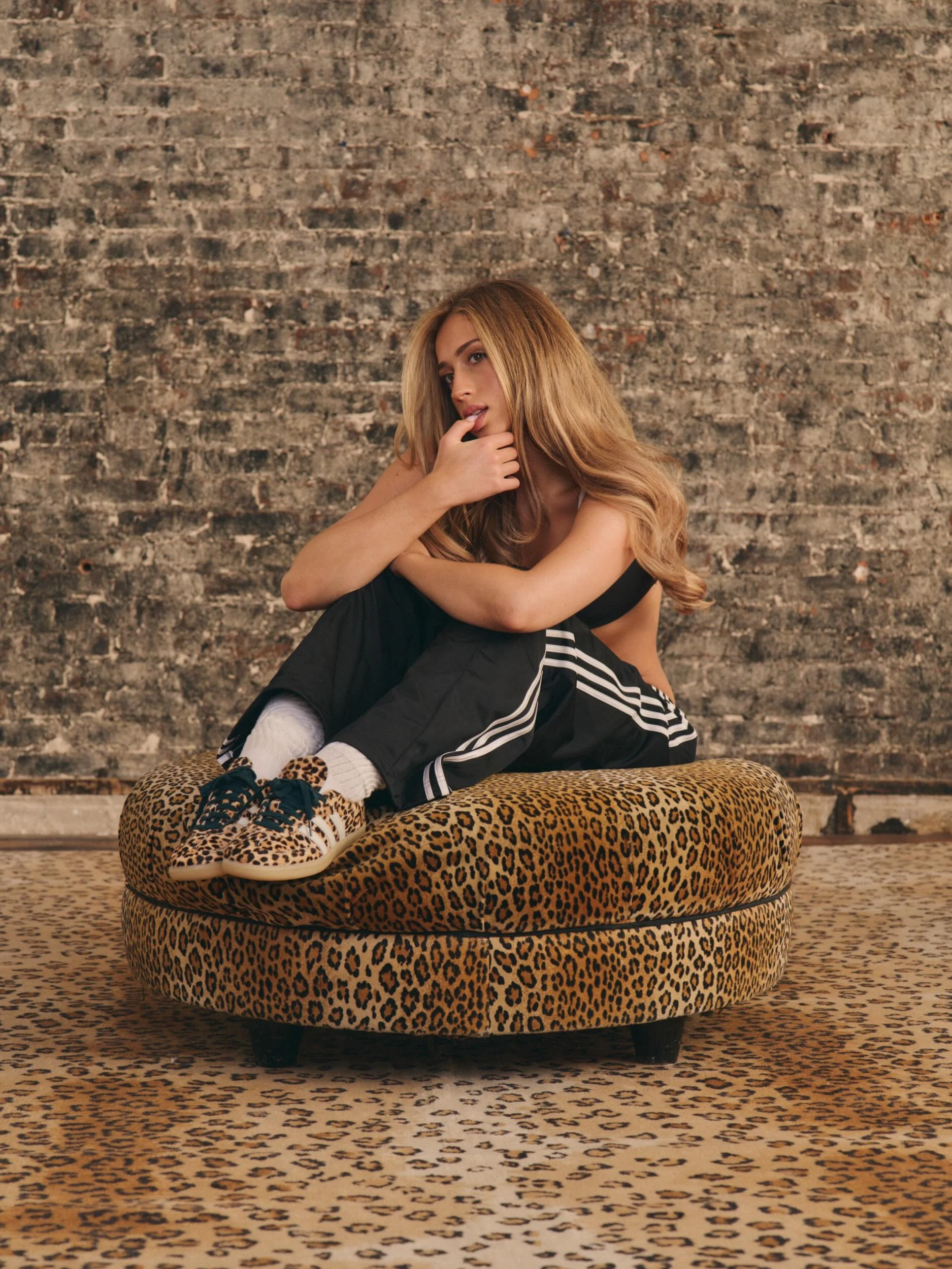 Black sports bra and track pants paired with white crew socks and leopard-print Adidas Sambas.