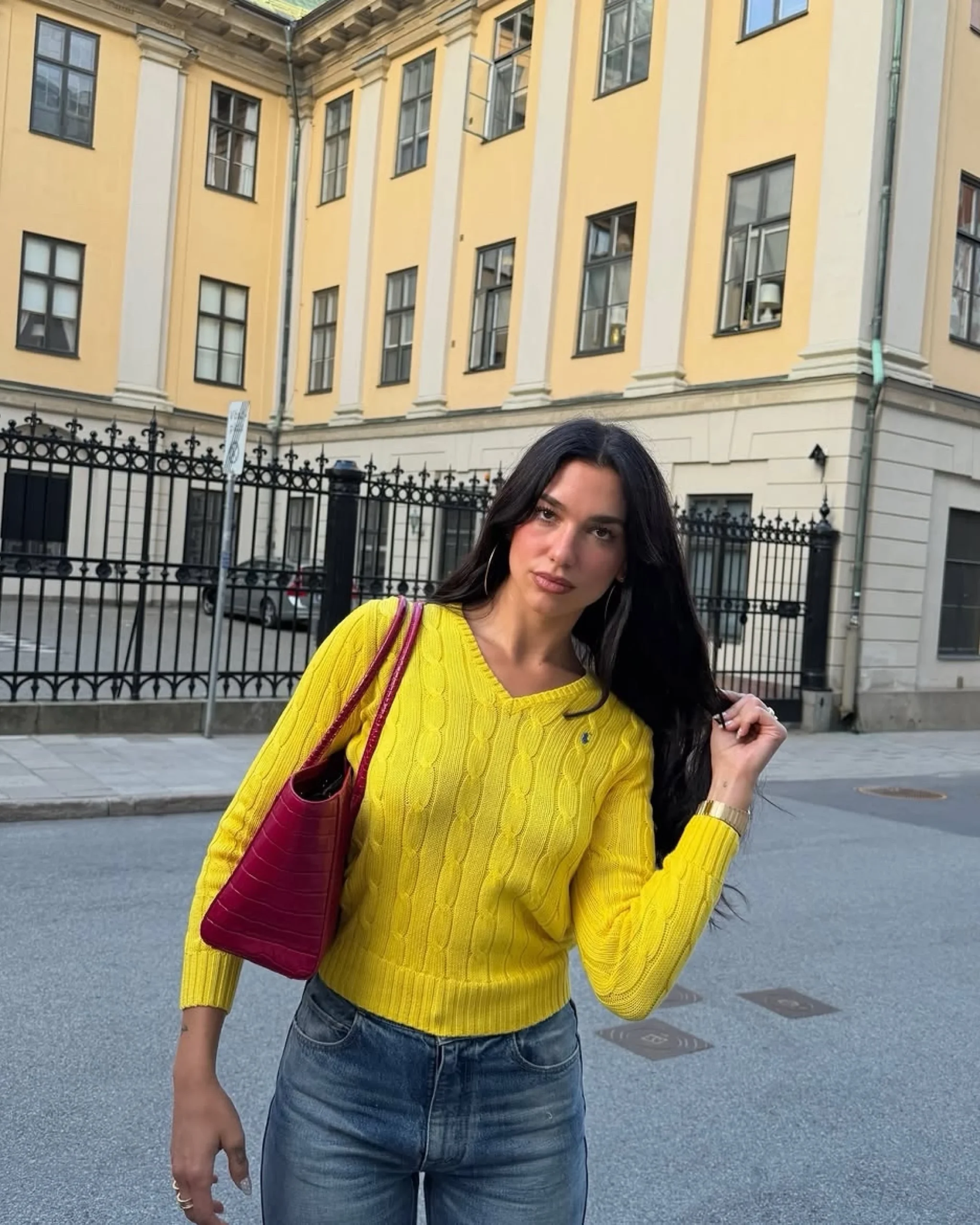Bright yellow cable knit V-neck sweater styled with blue jeans and a red textured shoulder bag.