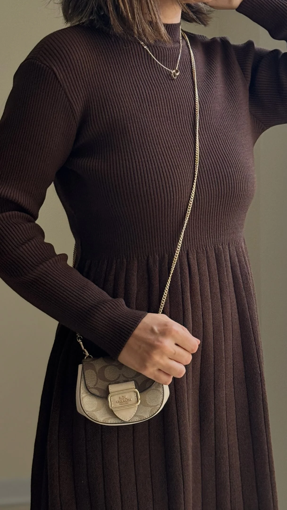 Dark brown ribbed high-neck midi dress styled with layered gold necklaces and a beige crossbody bag.