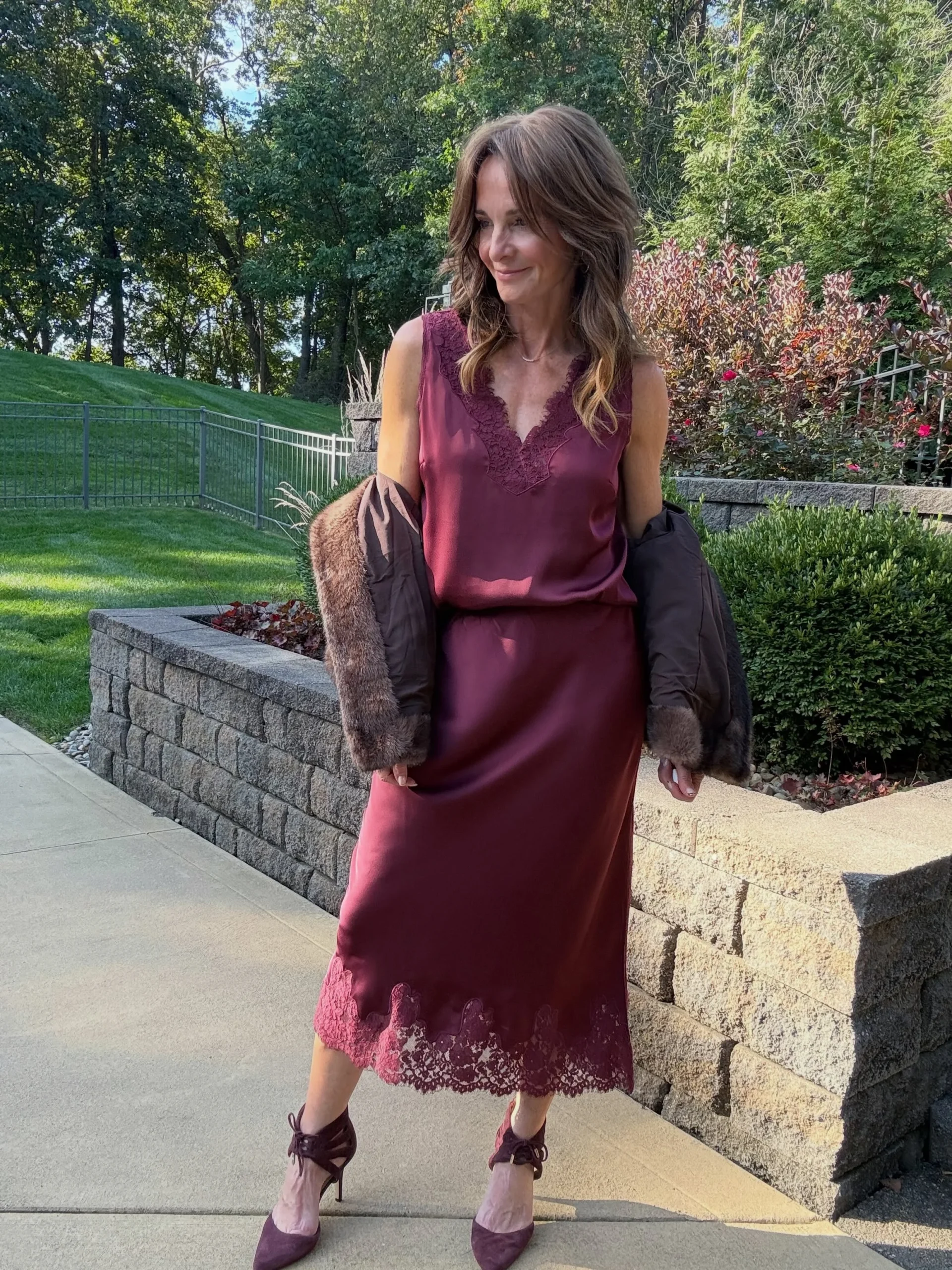 Burgundy lace-trim sleeveless midi dress with a dark fur-trimmed jacket draped over the arms.