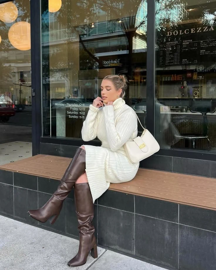 Cream turtleneck sweater dress worn with tall heeled brown boots and an ivory shoulder bag.
