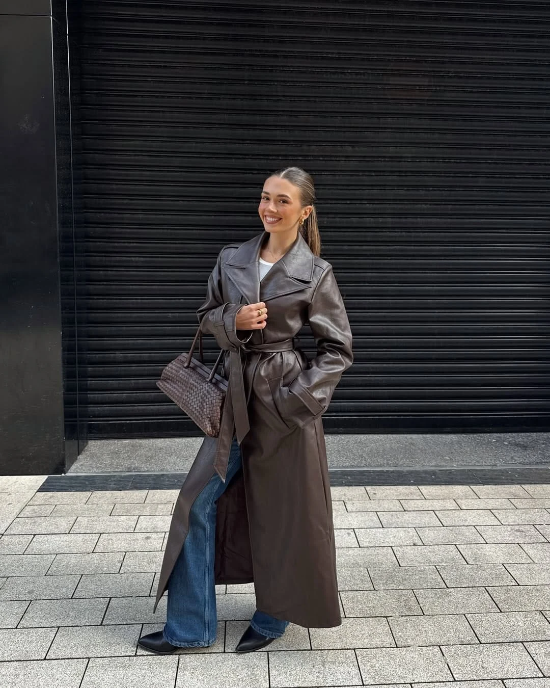 Espresso brown leather trench coat worn over a simple top, blue jeans, and sleek pointed boots.