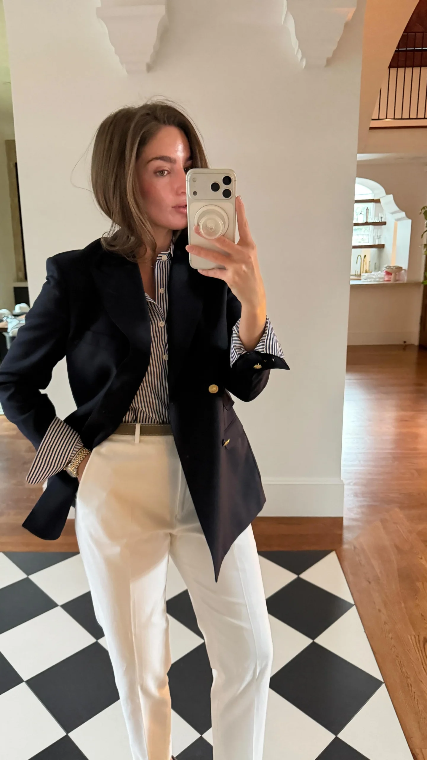 Navy blazer with gold buttons over a striped shirt and high-waisted white trousers with a pale belt.