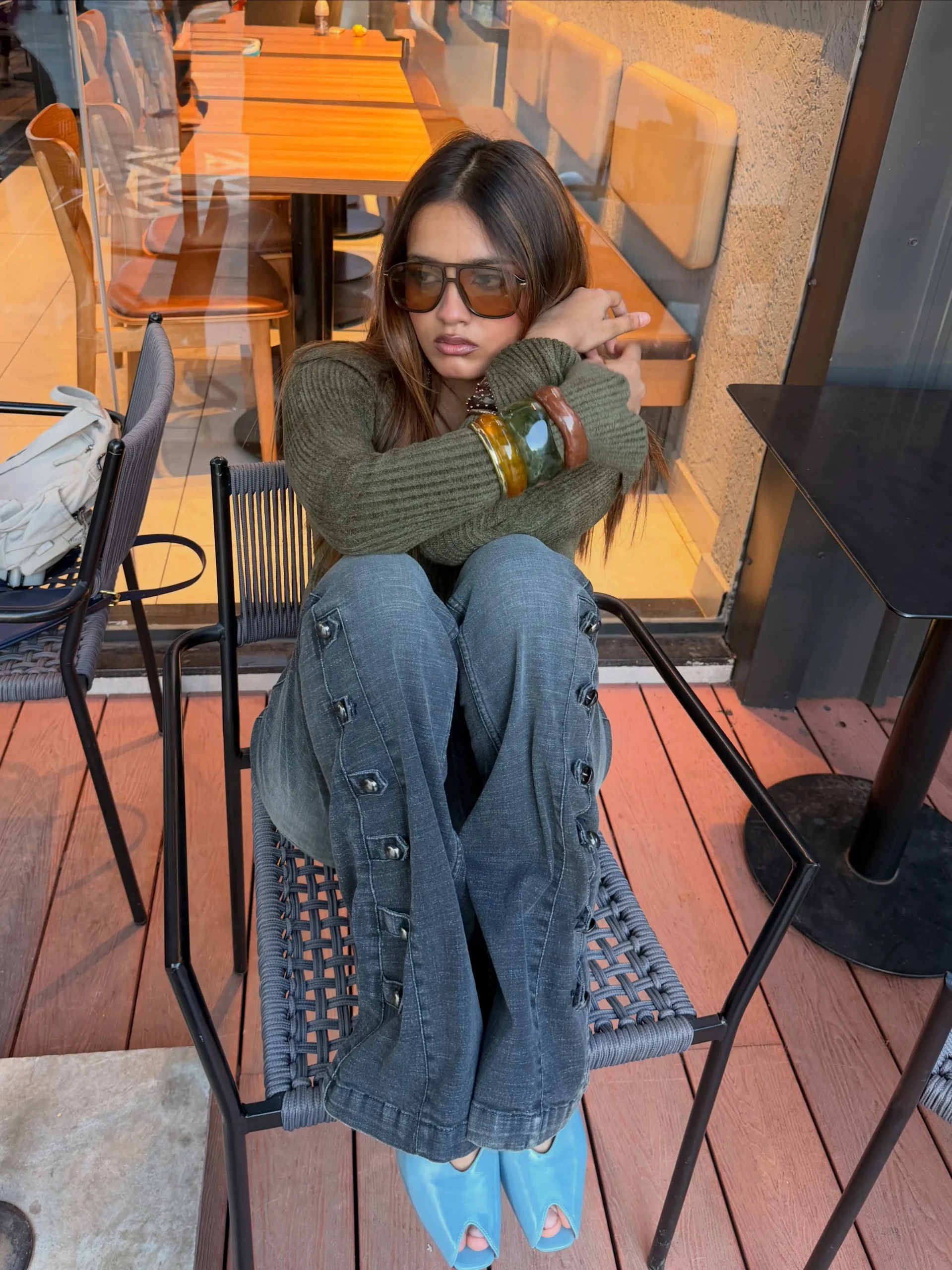 Dark olive ribbed sweater paired with embellished blue-gray jeans and bright blue open-toe shoes.