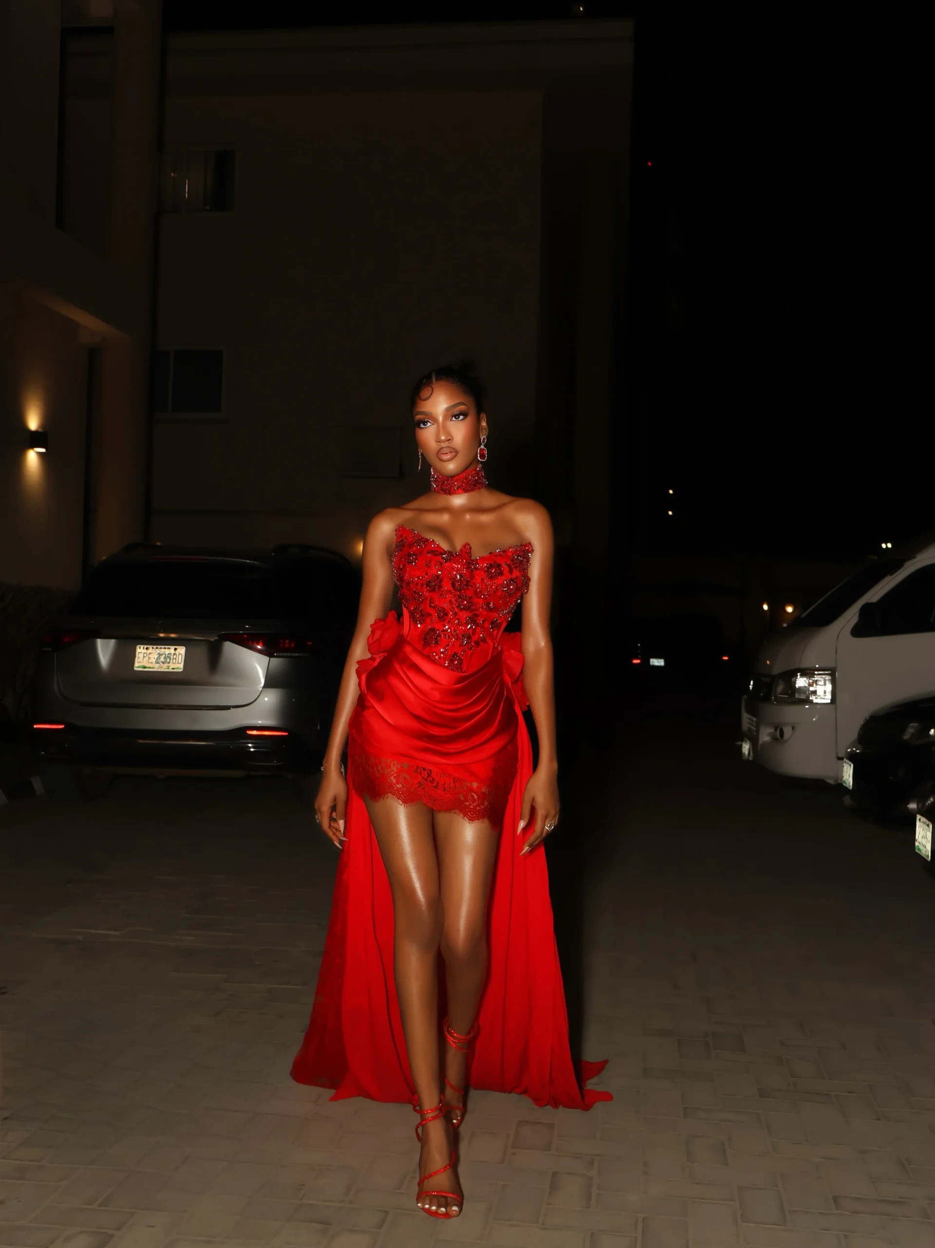 Strapless red gown with beaded bodice, draped mini skirt, long train, and heels.