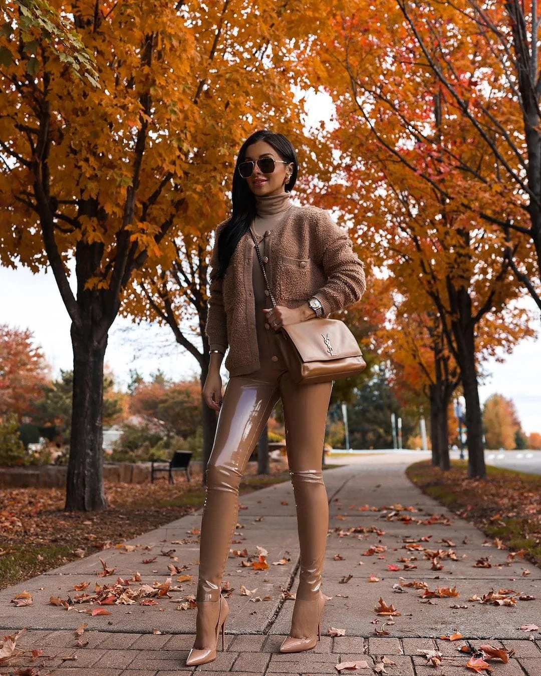 Woman in a warm-toned cardigan, brown leather pants, and brown pumps in a coordinated earthy outfit.