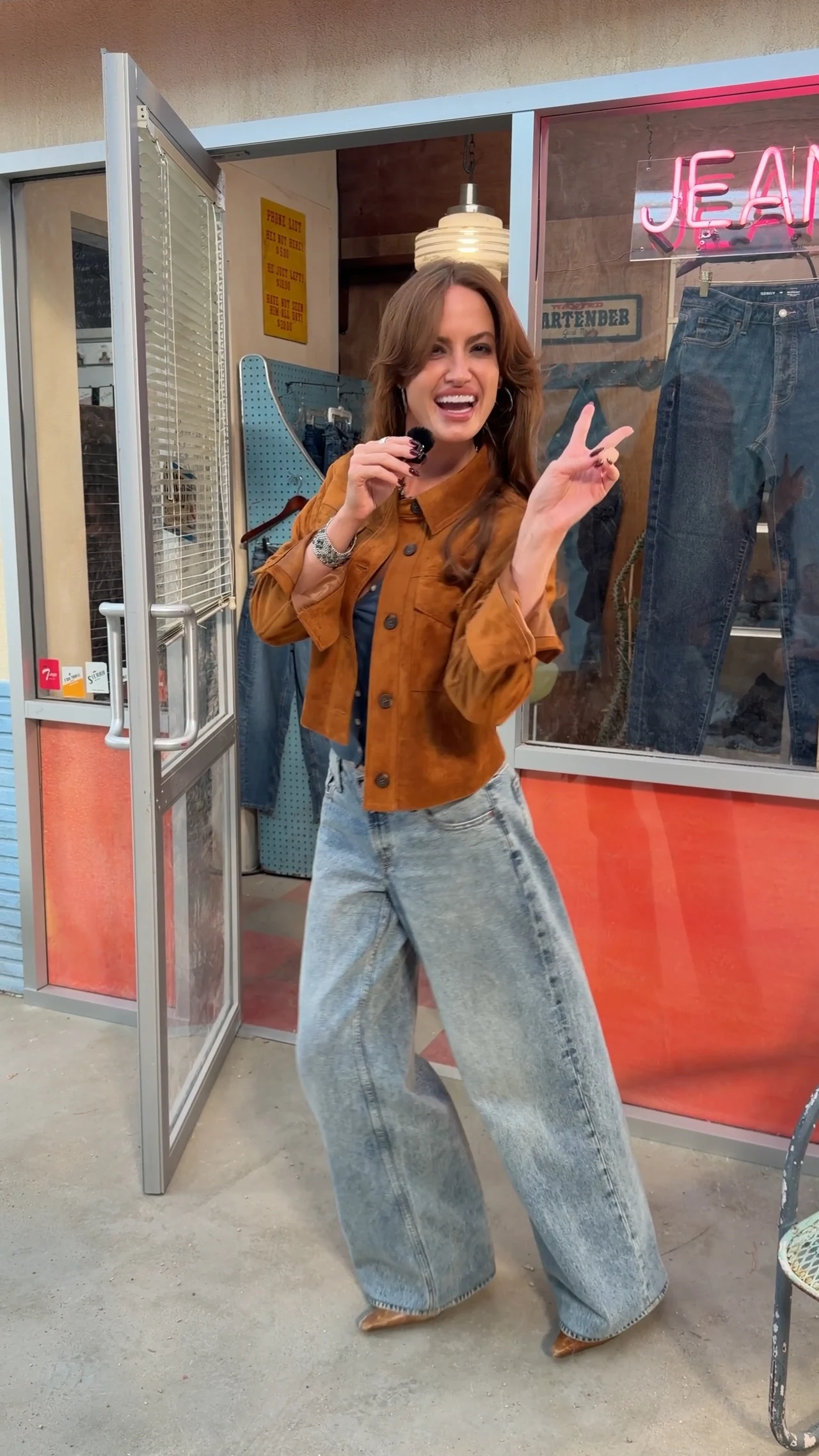Wide-leg baggy jeans styled with a blue top, brown cropped suede jacket, and pointed boots.