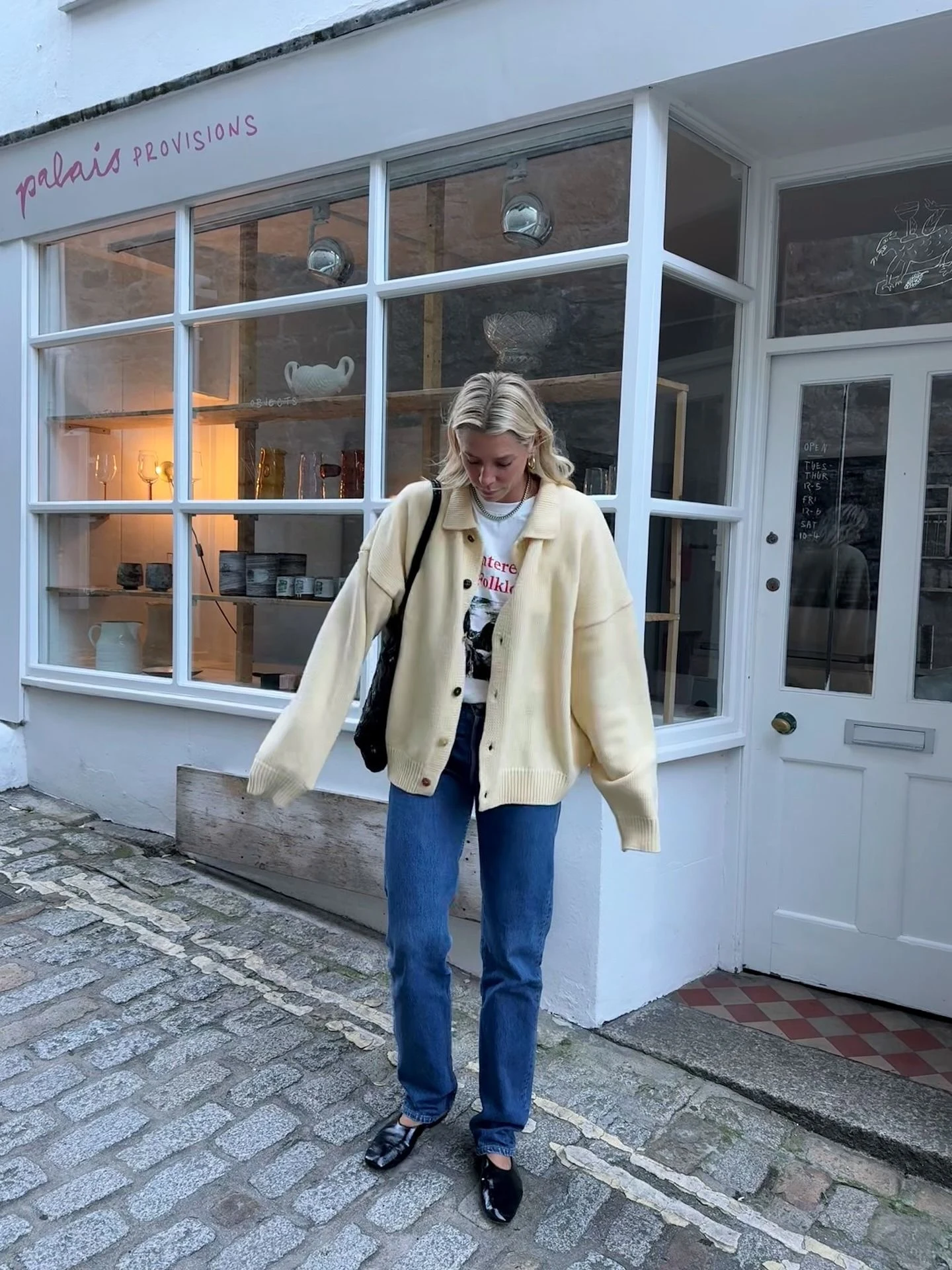 Woman in a yellow collared cardigan layered over a graphic tee and dark-wash jeans.