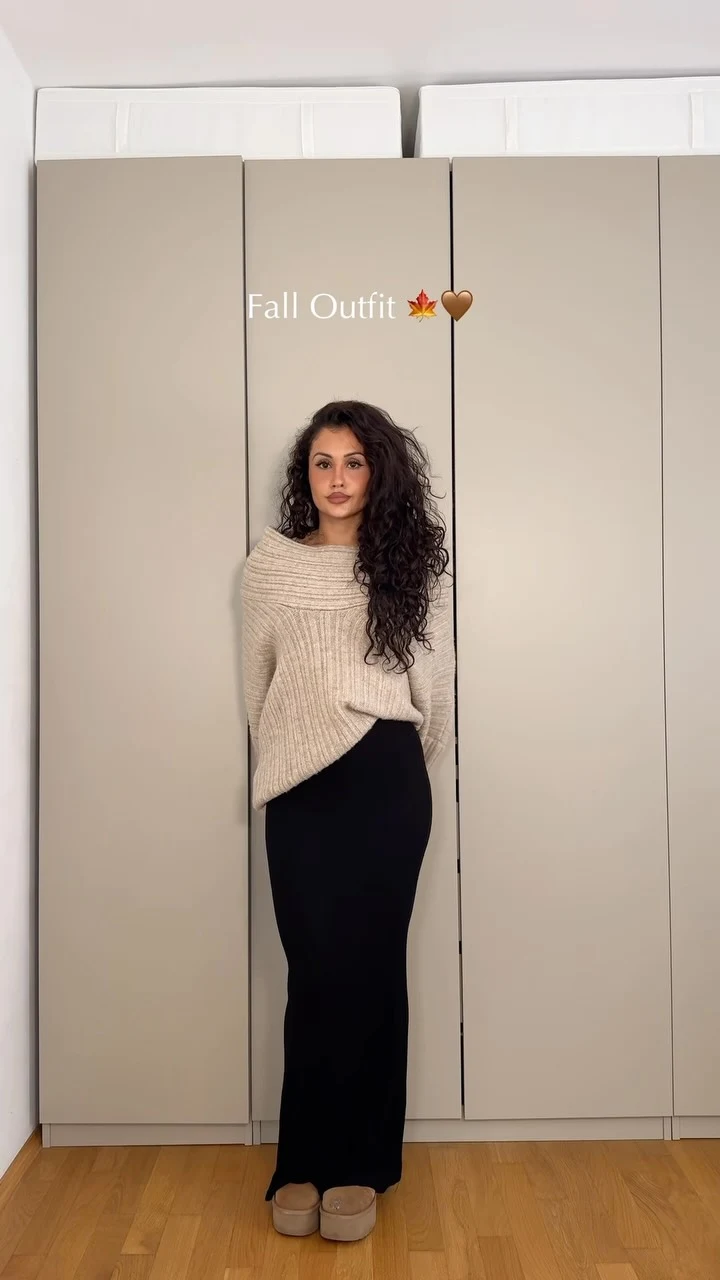 Woman in a black maxi dress layered with a beige chunky-knit sweater and tan platform shoes.