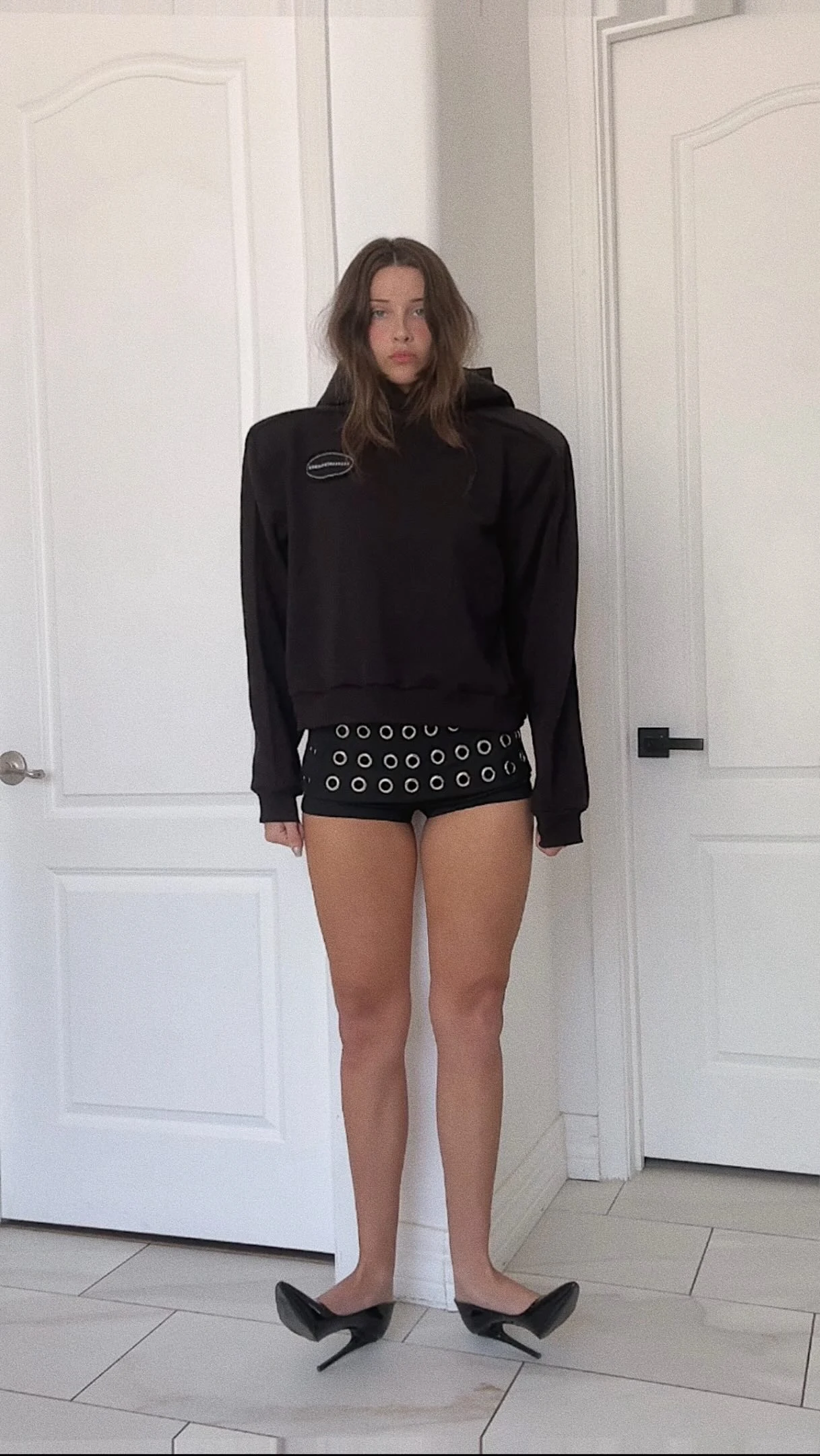 Oversized black sweatshirt worn with eyelet-trimmed black shorts and black pointed-toe heels.