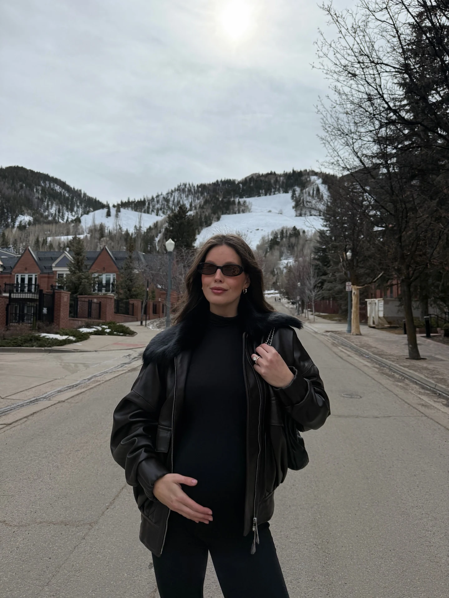 Person in black turtleneck, black pants, shiny fur-collar jacket, and narrow dark sunglasses.