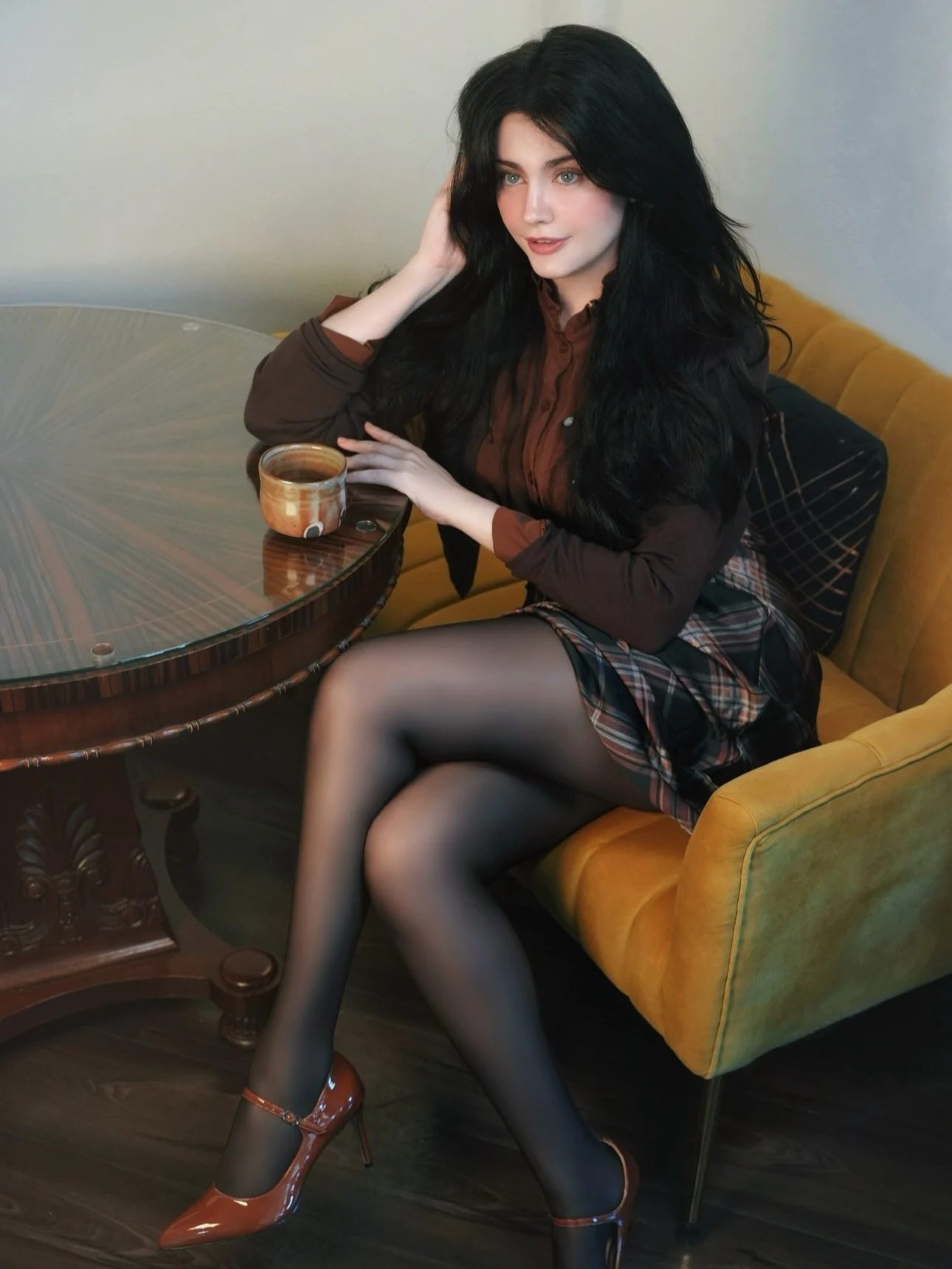 Model in a dark brown ruffled blouse, plaid mini skirt, sheer black tights, and ankle-strap heels.
