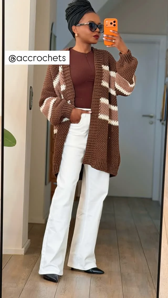 Long brown striped crochet cardigan over a burgundy top, white wide-leg trousers, and black pointed shoes.