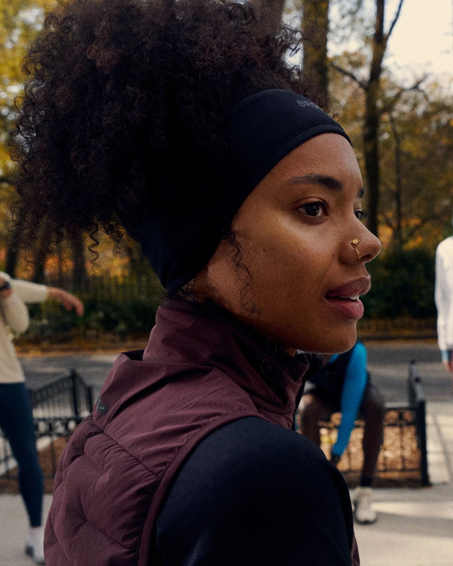 Close-up of a person in a burgundy quilted vest over a black long-sleeve top with a wide black headband.