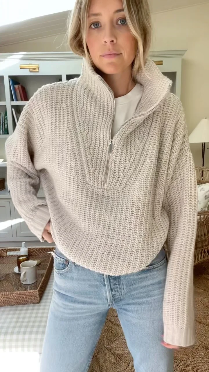 Chunky beige half-zip ribbed sweater layered over a white top with light-wash blue jeans.