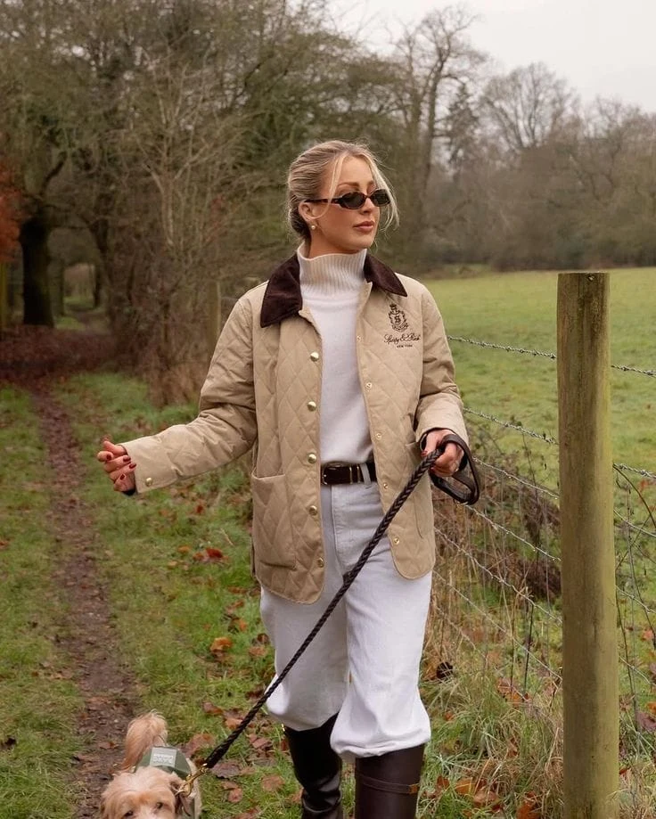 Cream turtleneck and white jodhpurs under a beige quilted jacket with brown collar and riding boots.