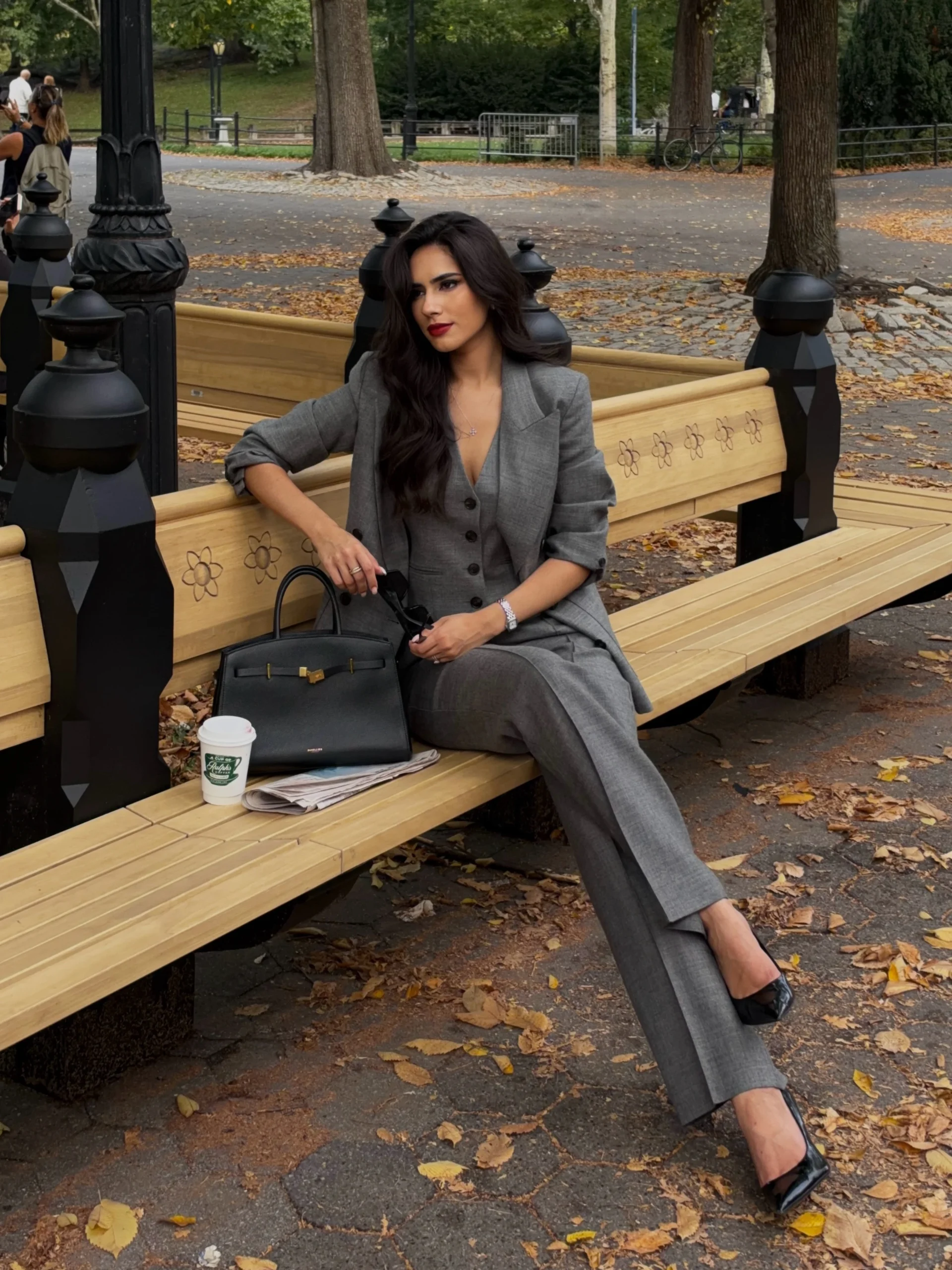 Woman in a matching gray blazer and trousers with black pointed shoes and a structured black handbag.