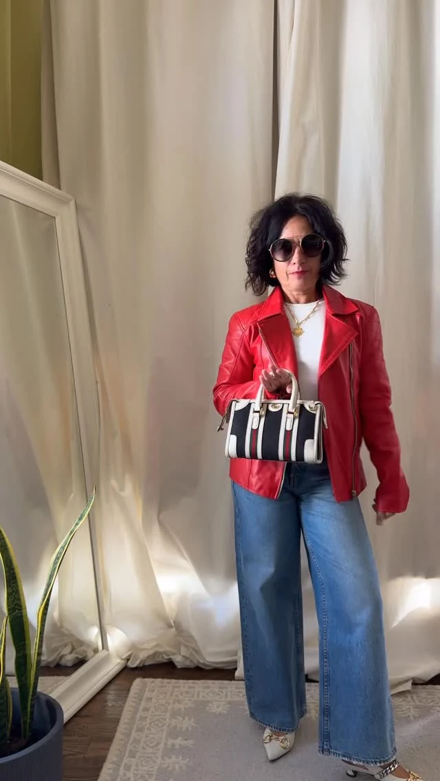 Red leather biker jacket zipped over white ribbed top, light-wash wide-leg jeans, and gold sunglasses.