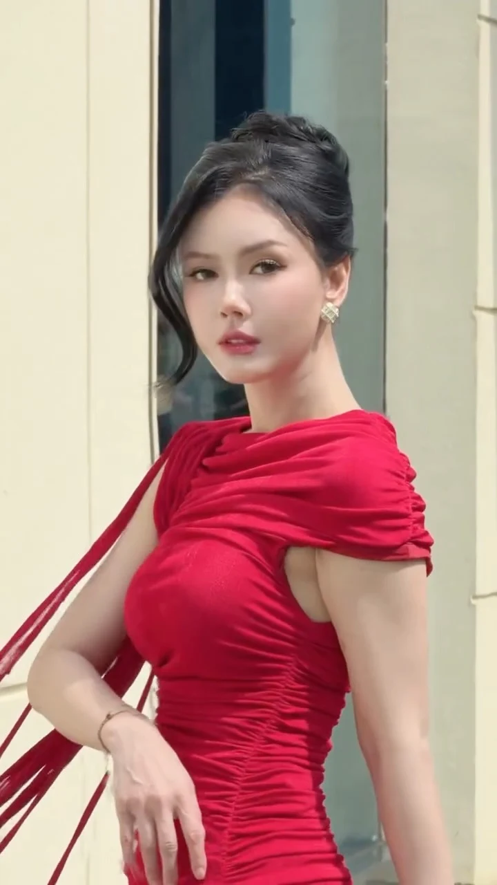 Woman in a vivid cherry-red ruched asymmetrical dress with draped shoulder detail and gold earrings.