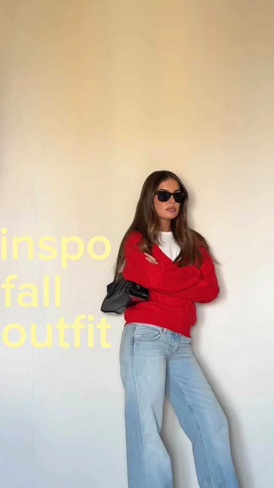Red V-neck sweater over a white top, light-wash flared jeans, black shoulder bag, and dark sunglasses.
