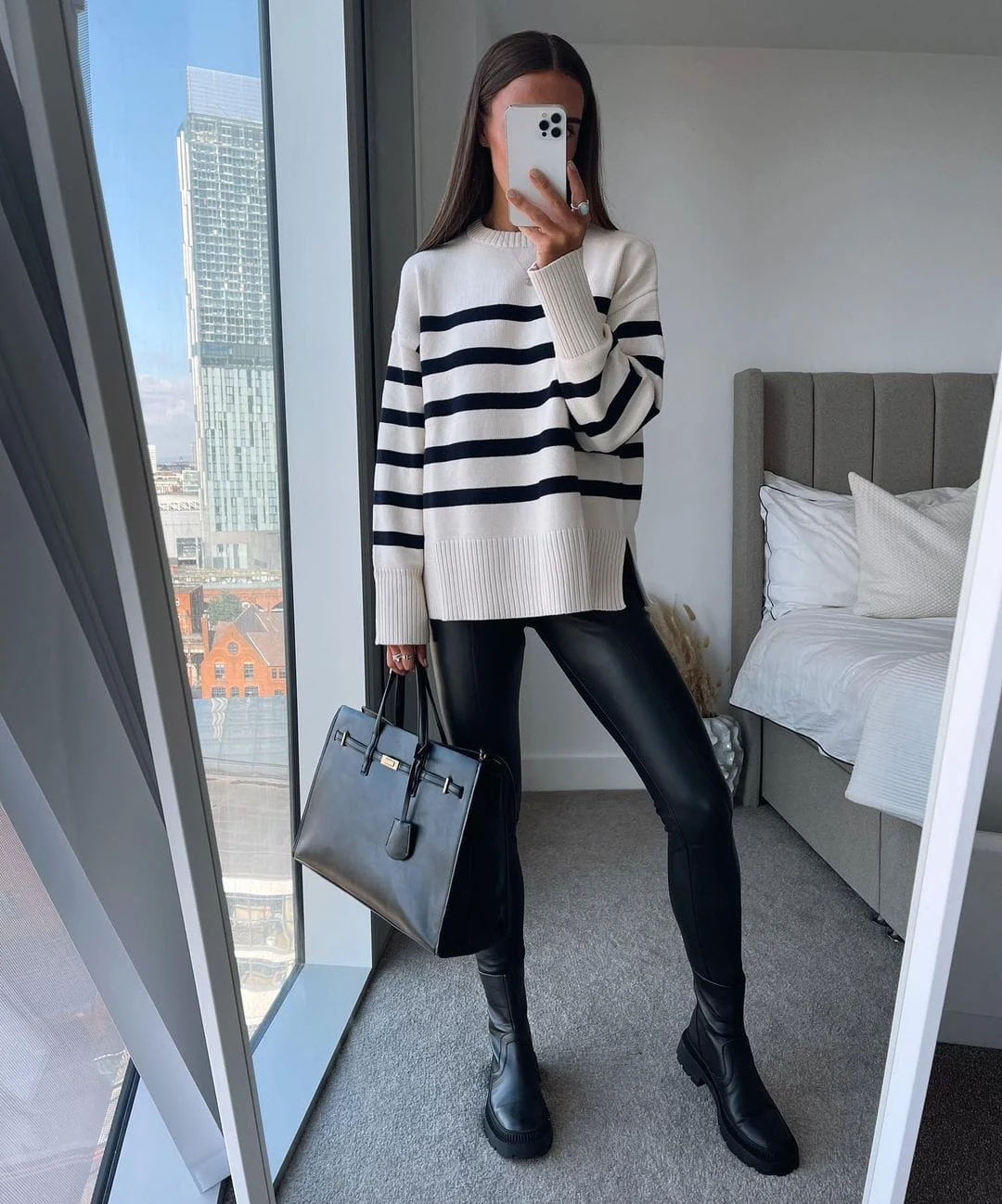 Woman wearing a striped sweater, black leather pants, and Chelsea boots in a casual fashionable outfit.