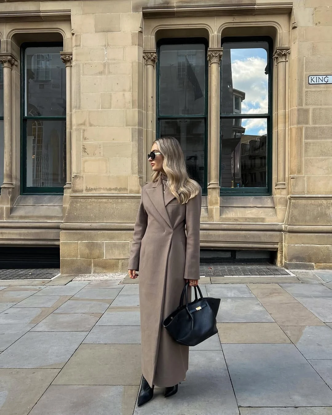 Taupe wool long coat over a matching maxi dress with pointed black boots and a structured handbag.