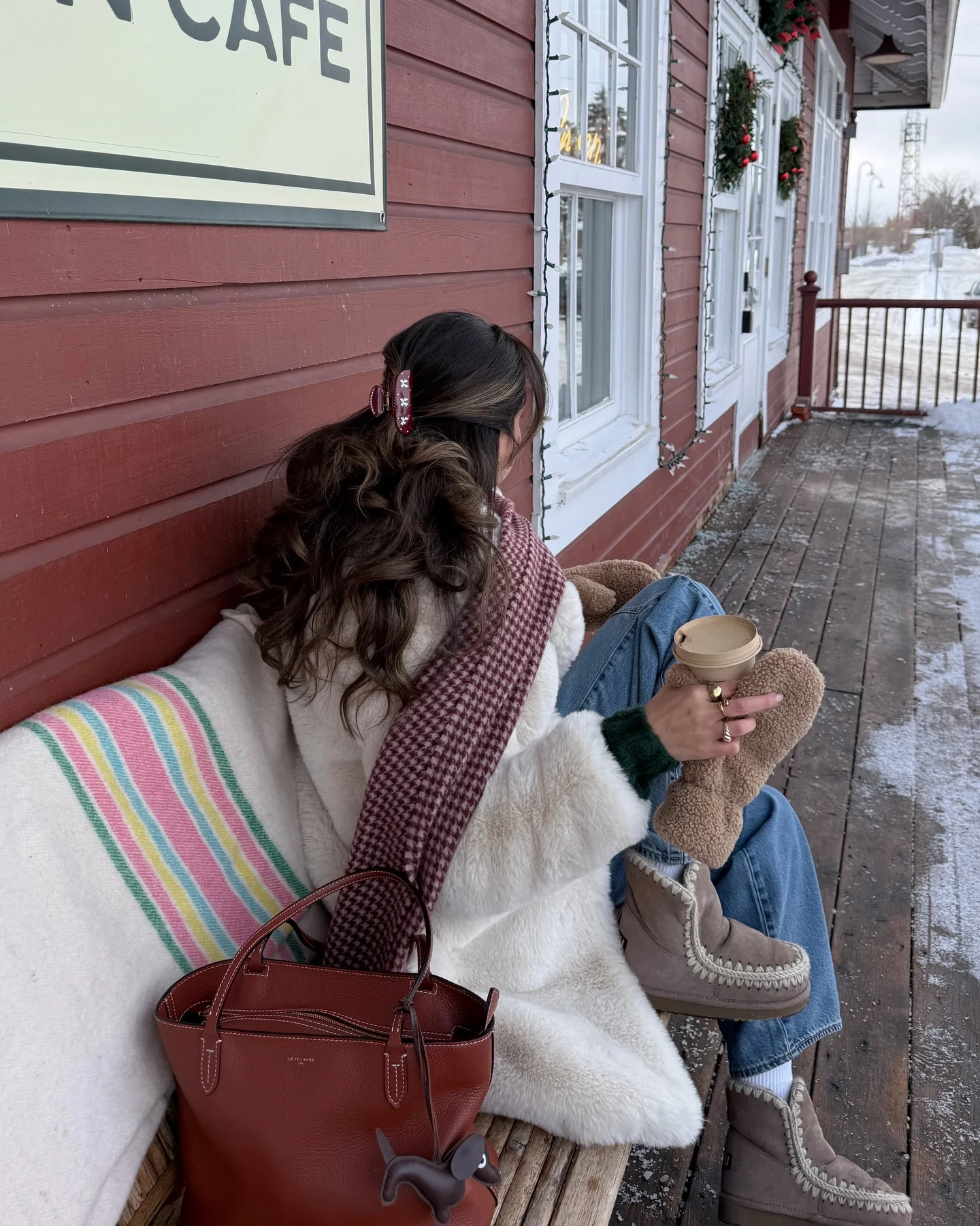 White faux fur coat layered over a green knit, wide leg jeans, and tan shearling boots.