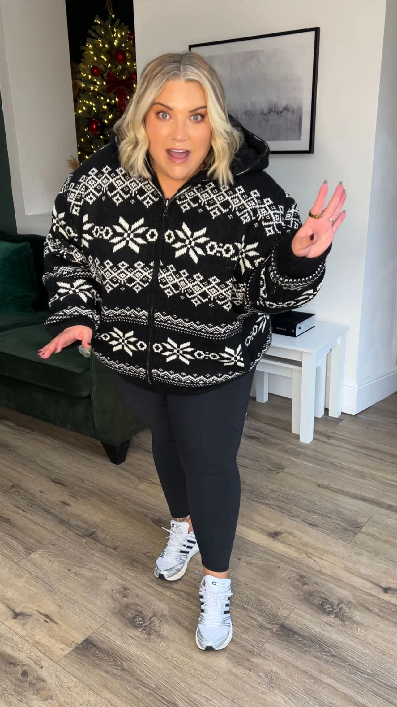 Black hooded snowflake-print zip jacket worn with black leggings and white athletic shoes near a Christmas tree.