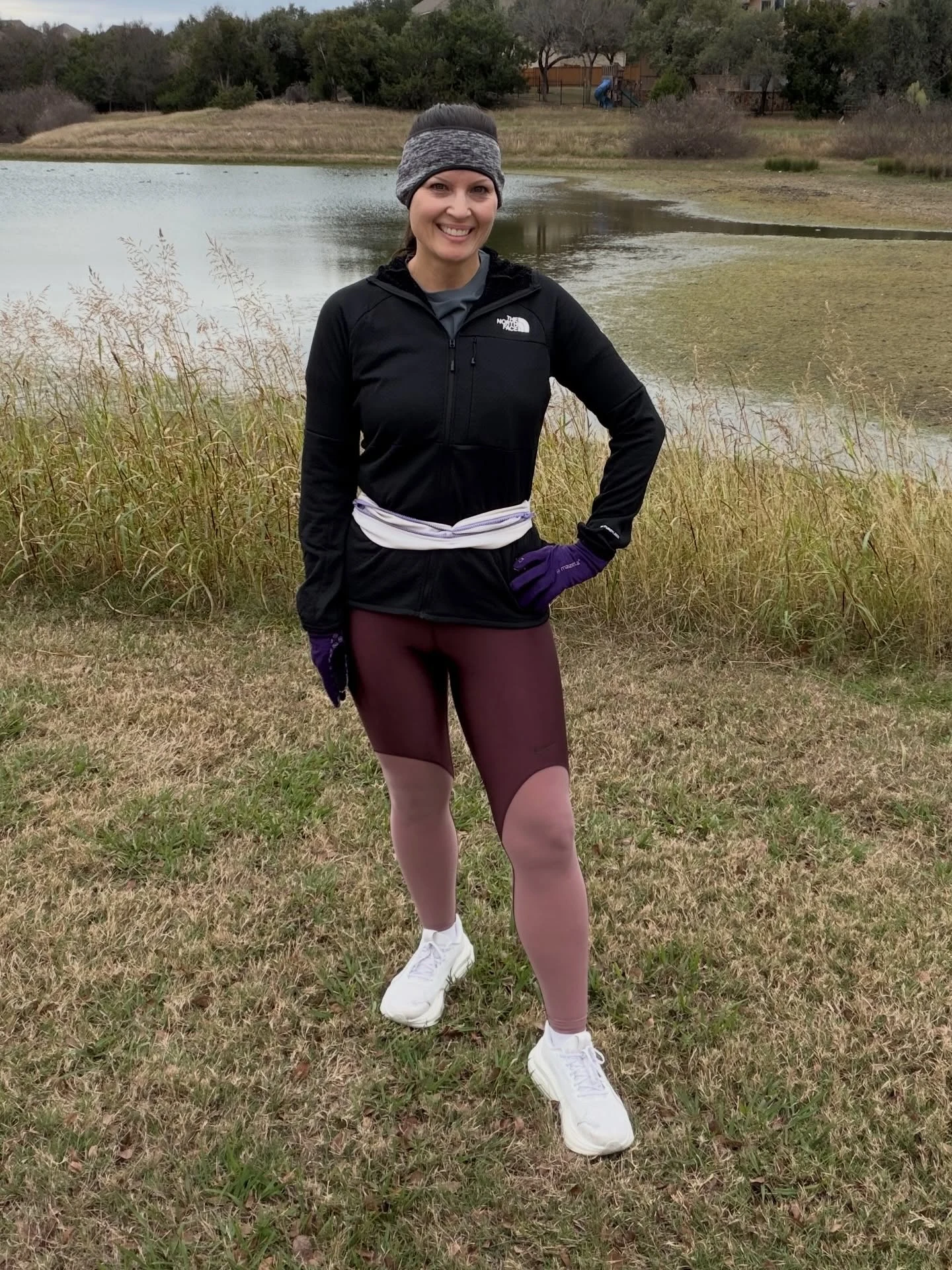 Person in a black zip jacket, burgundy shorts, purple gloves, gray headband, and white athletic shoes.