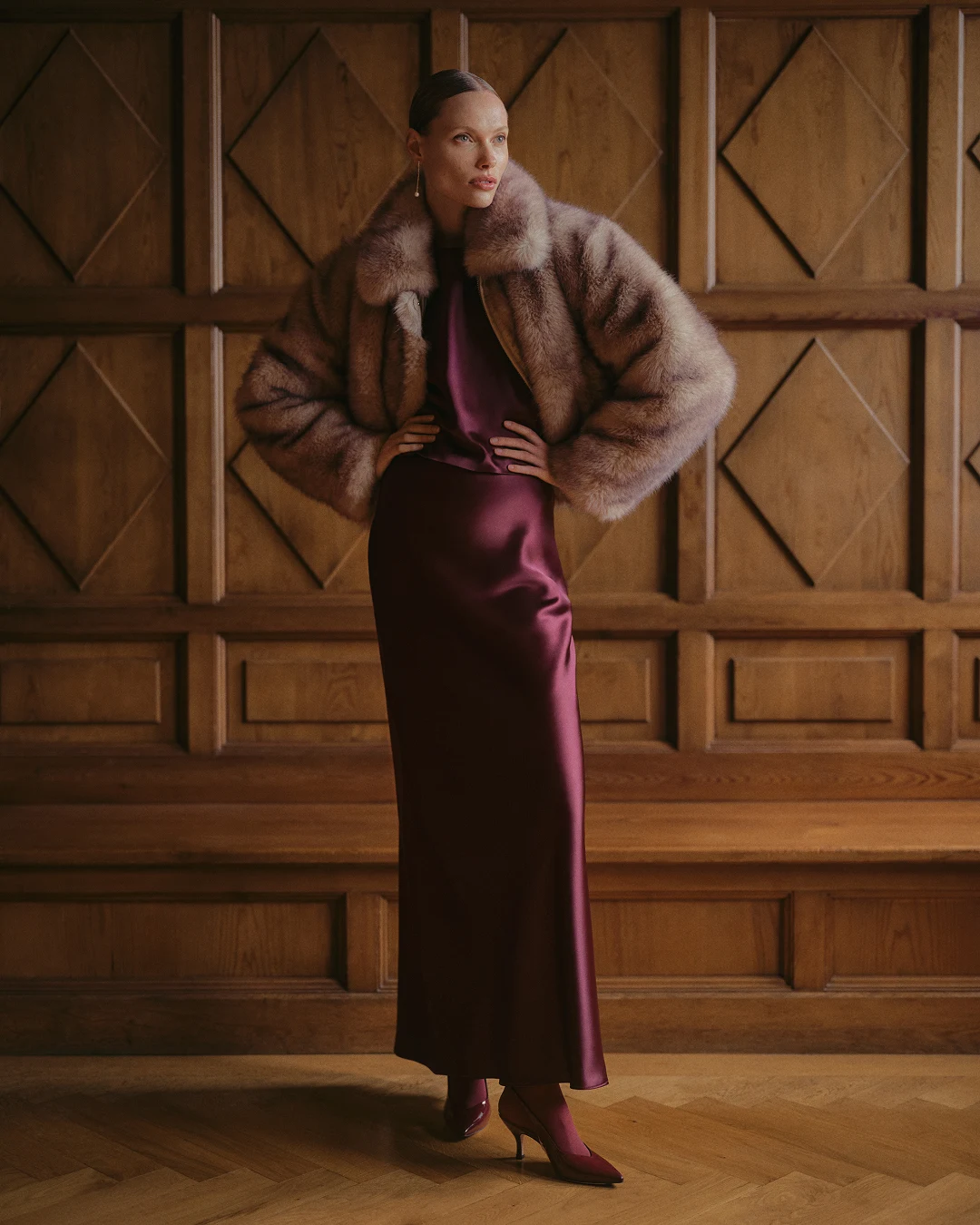 Long glossy burgundy slip dress with a cropped voluminous taupe fur jacket and matching pointed-toe heels.